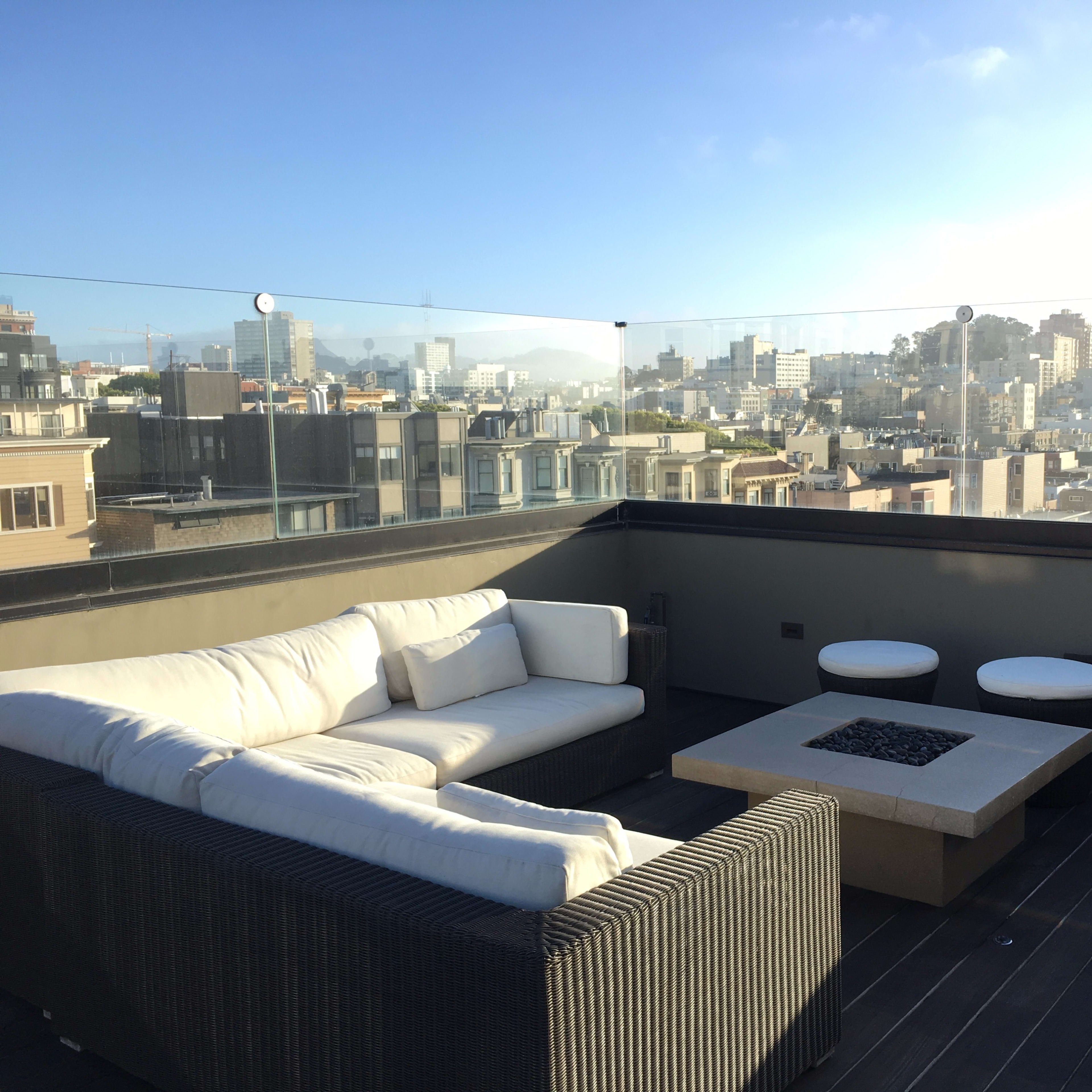 A rooftop terrace features a modern sectional sofa, a fire pit, and city skyline views.