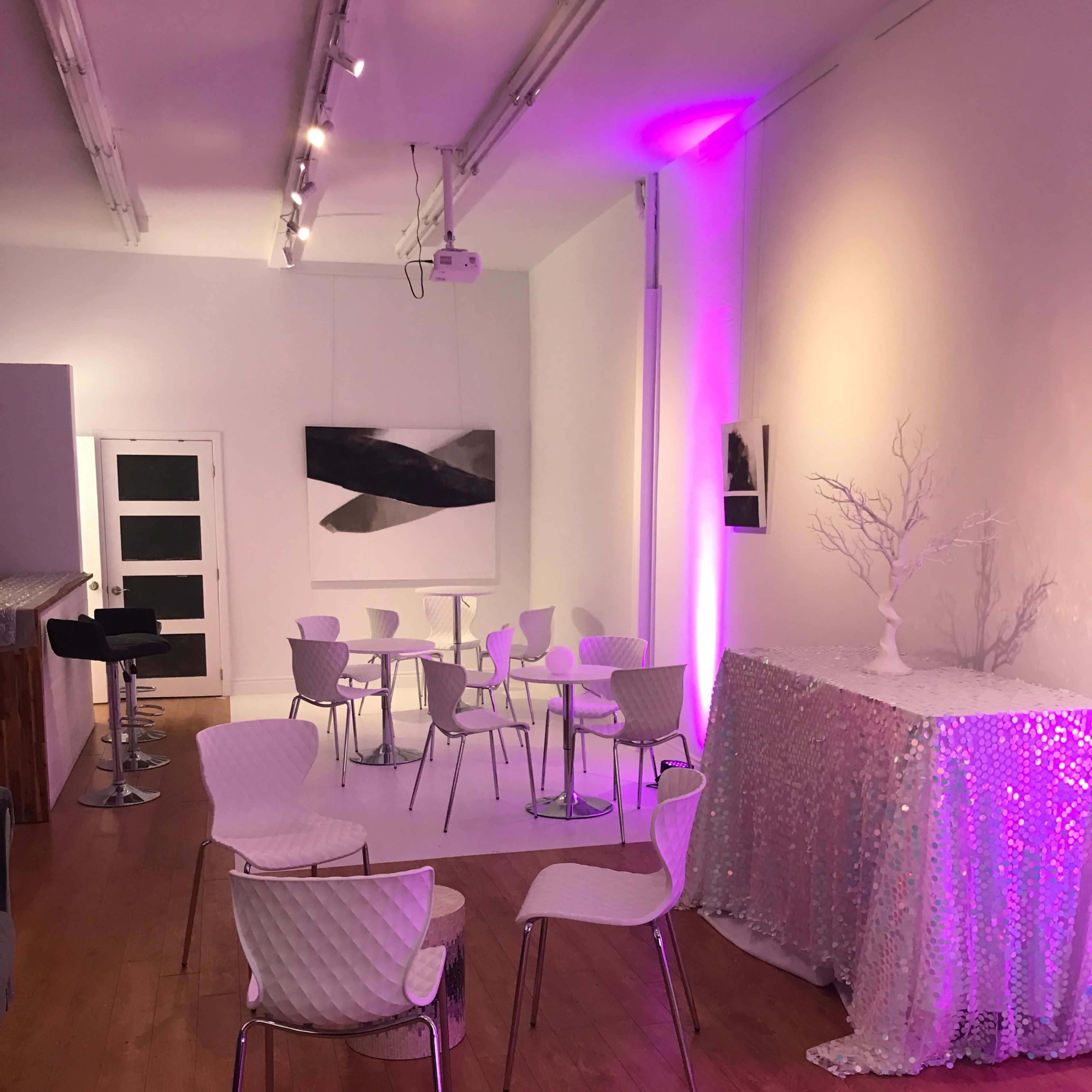 A modern, minimalist interior with several white chairs and tables, illuminated by soft purple lighting.