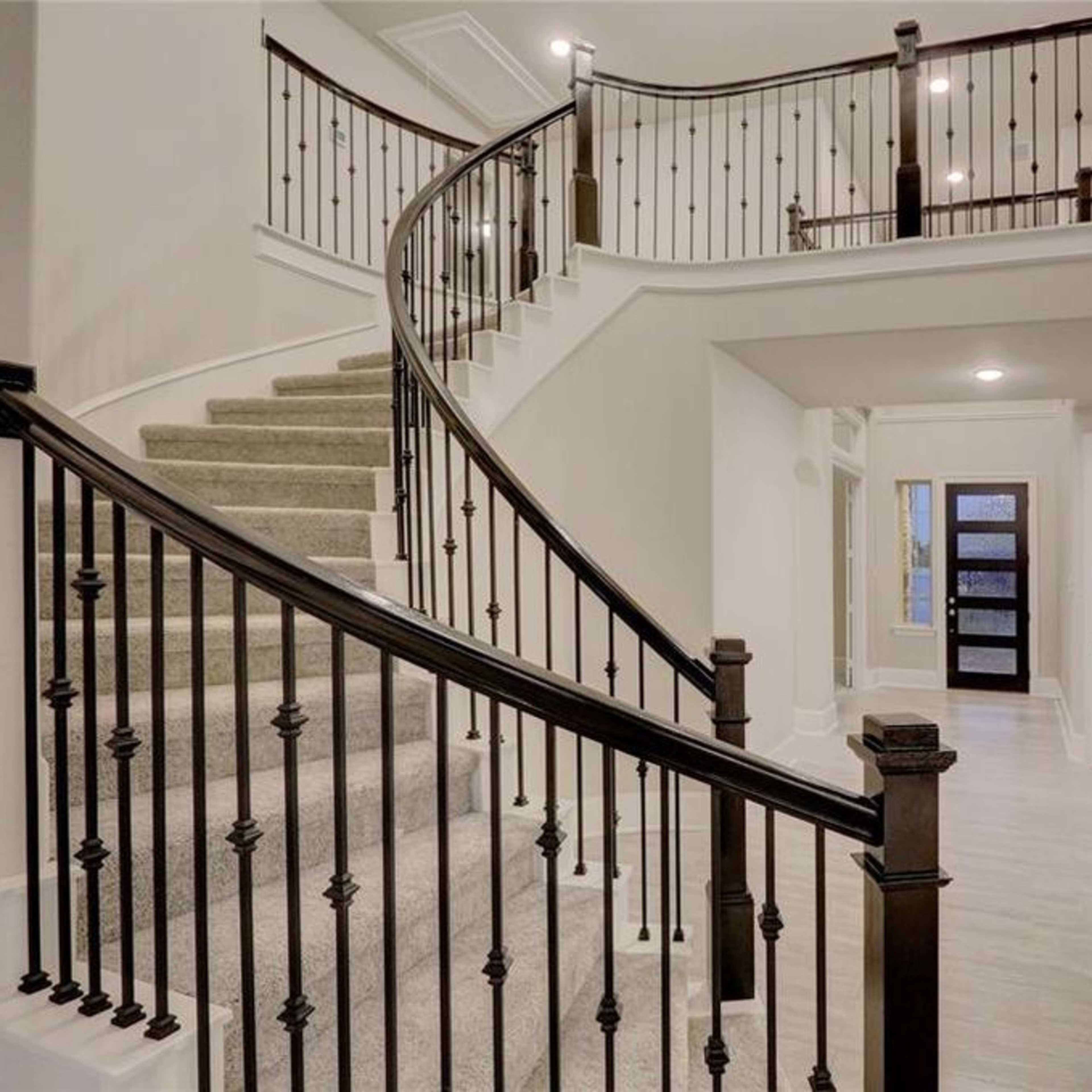 A spiral staircase with black wrought iron railings leads to a second level in a spacious foyer with light-colored walls and wood flooring.