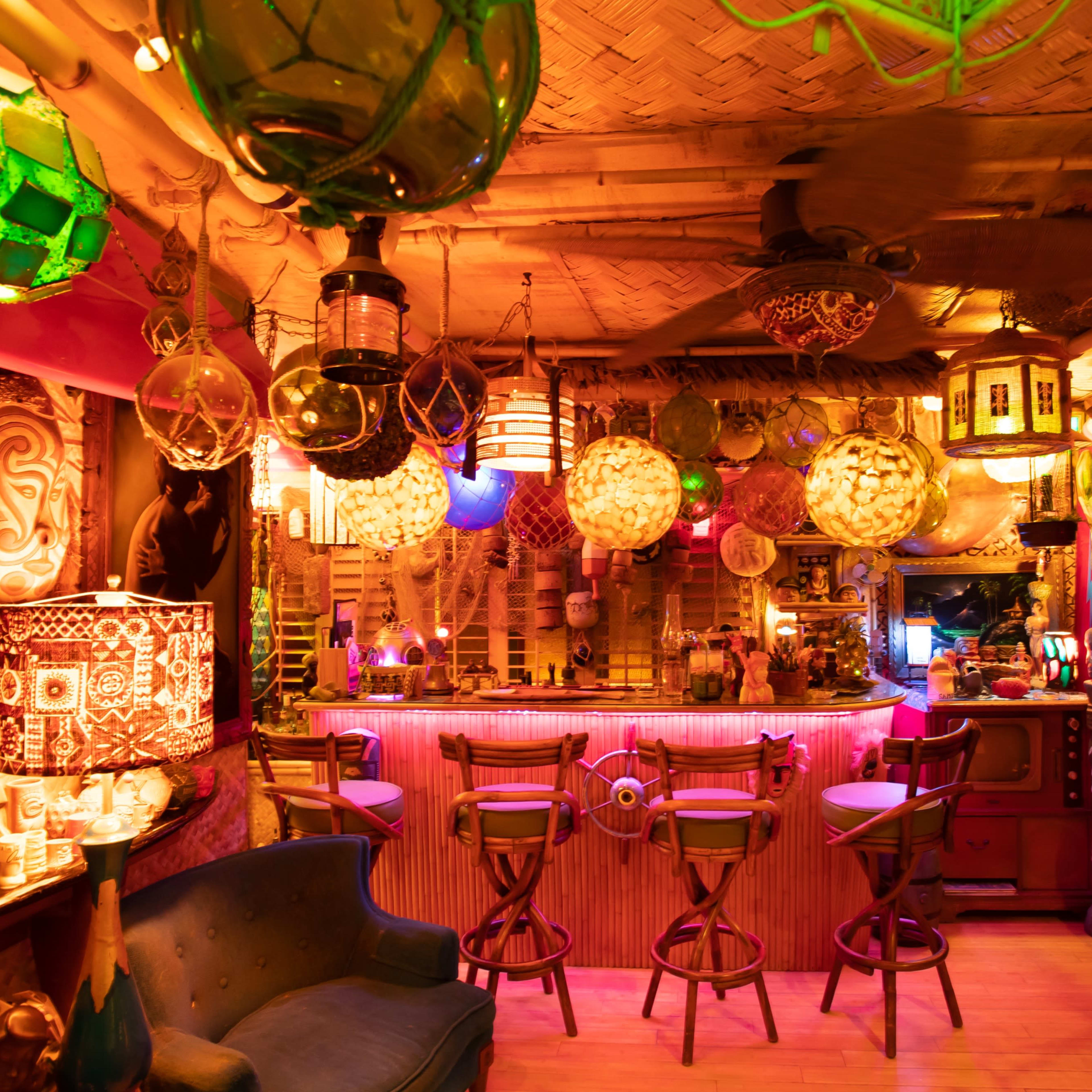 A vibrant tiki-themed bar with colorful lanterns, a circular bar counter, and various decorations on the walls.