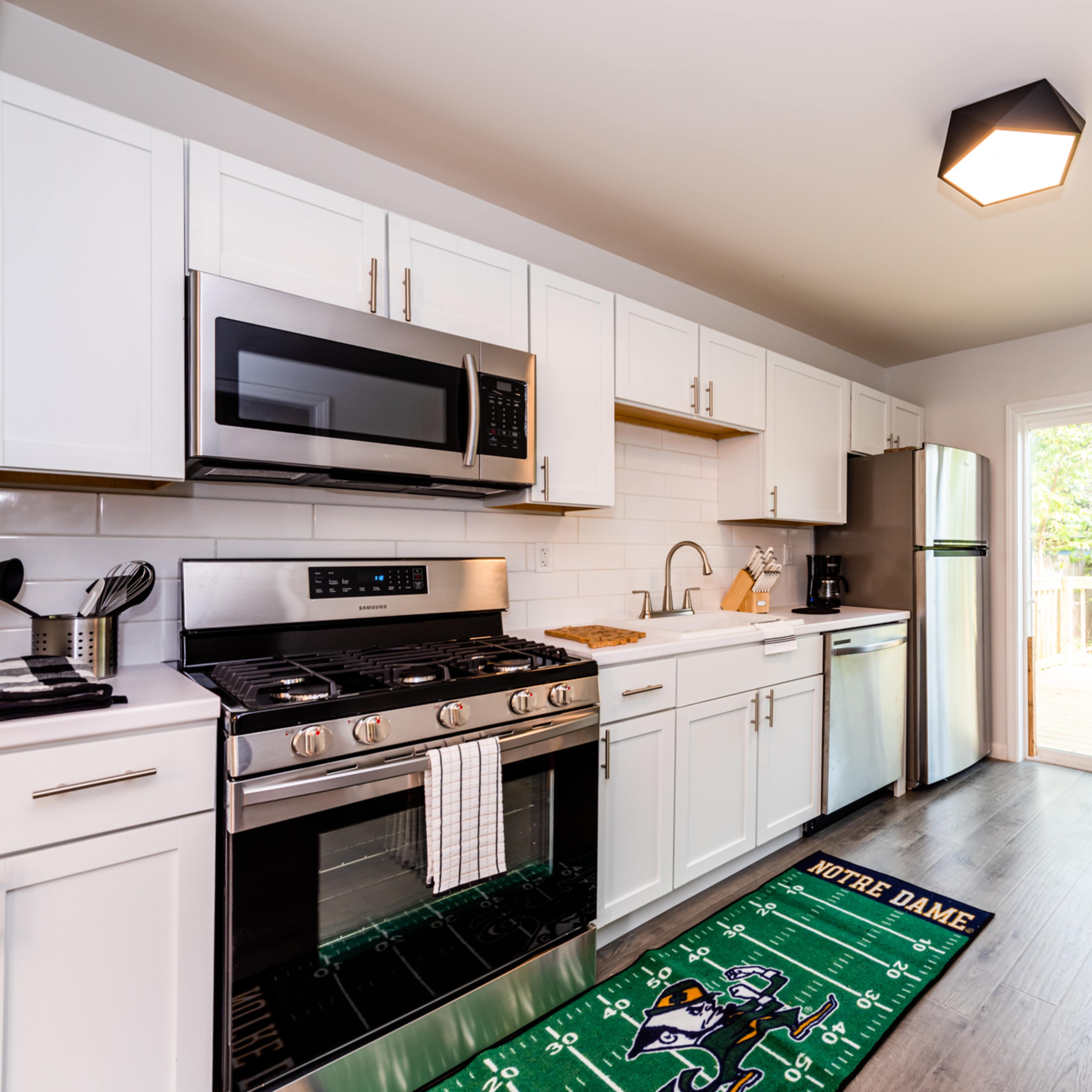 A modern kitchen features white cabinets, stainless steel appliances, and a dining area with a sliding glass door opening to a deck.