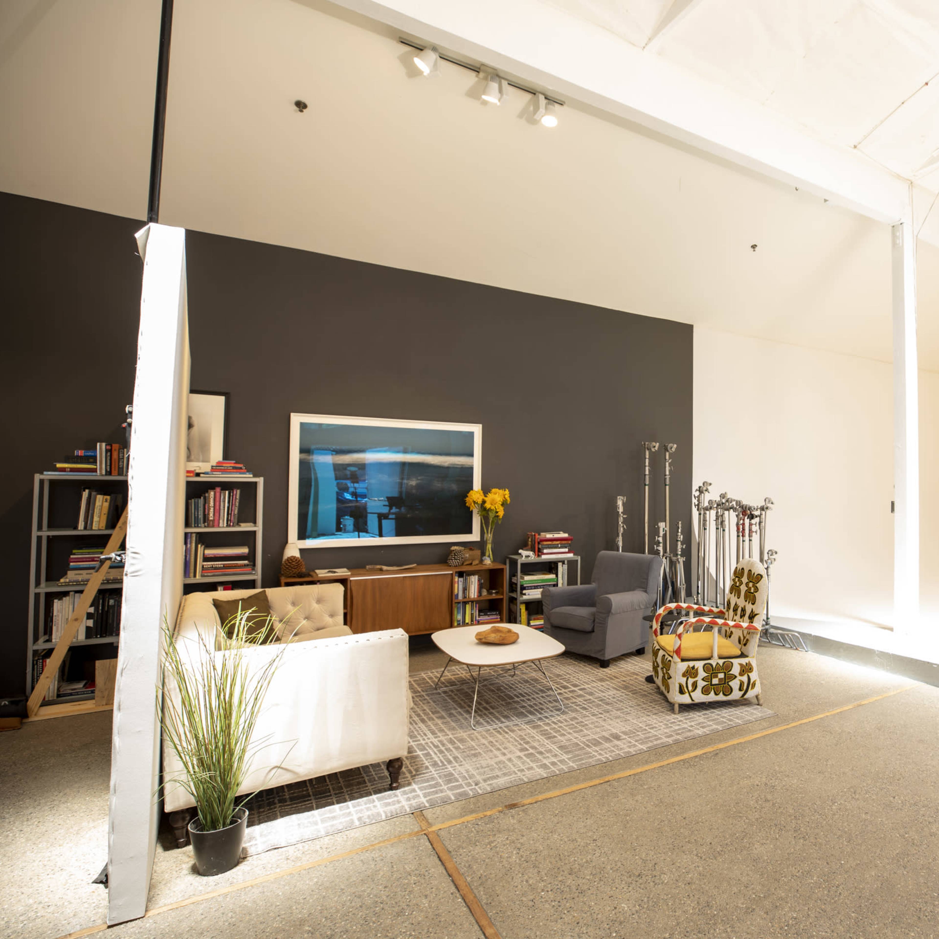 A spacious studio featuring a gray accent wall, a white sofa, a wooden coffee table, and a gray armchair, along with bookshelves and decorative items.