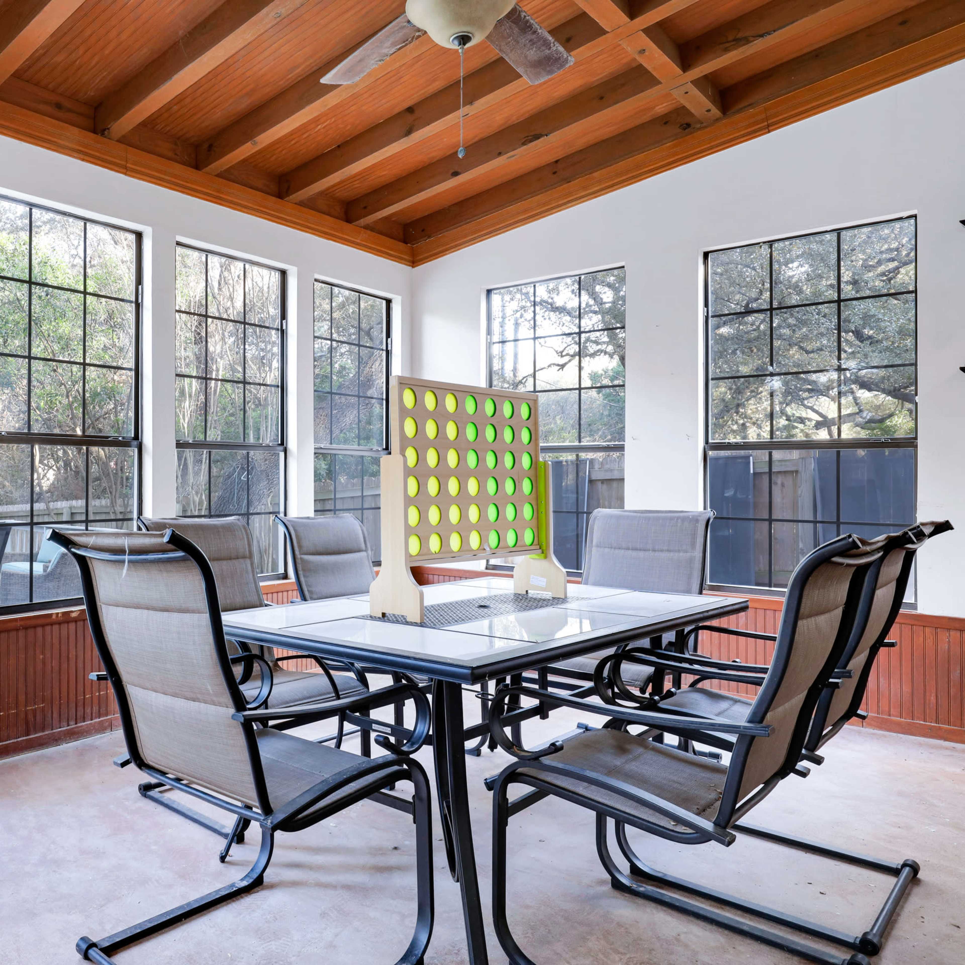 A screened-in patio features a table surrounded by six chairs, with a door leading to an outdoor pool area and large windows allowing ample light.