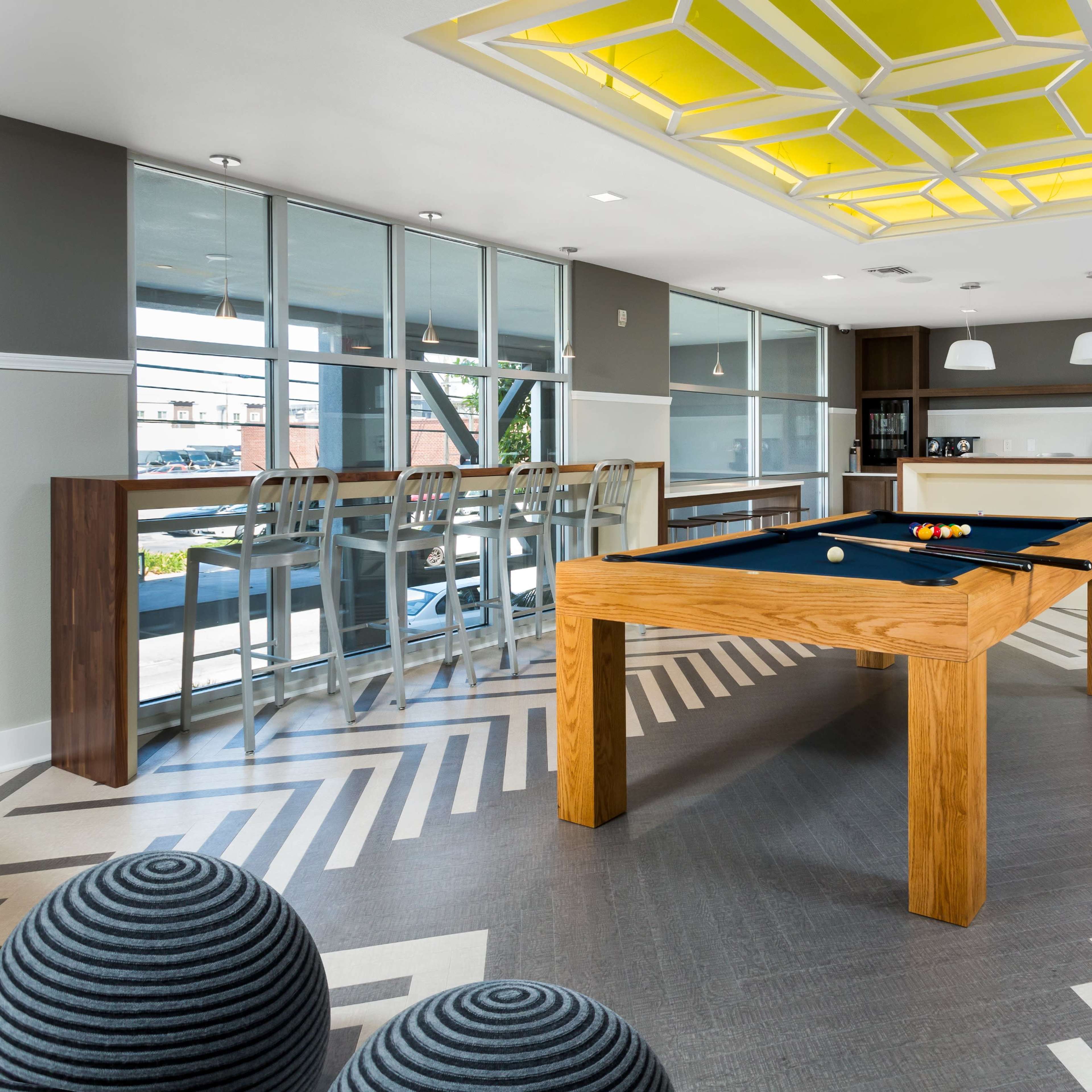 A modern game room with a pool table, bar seating, and stylish geometric flooring.
