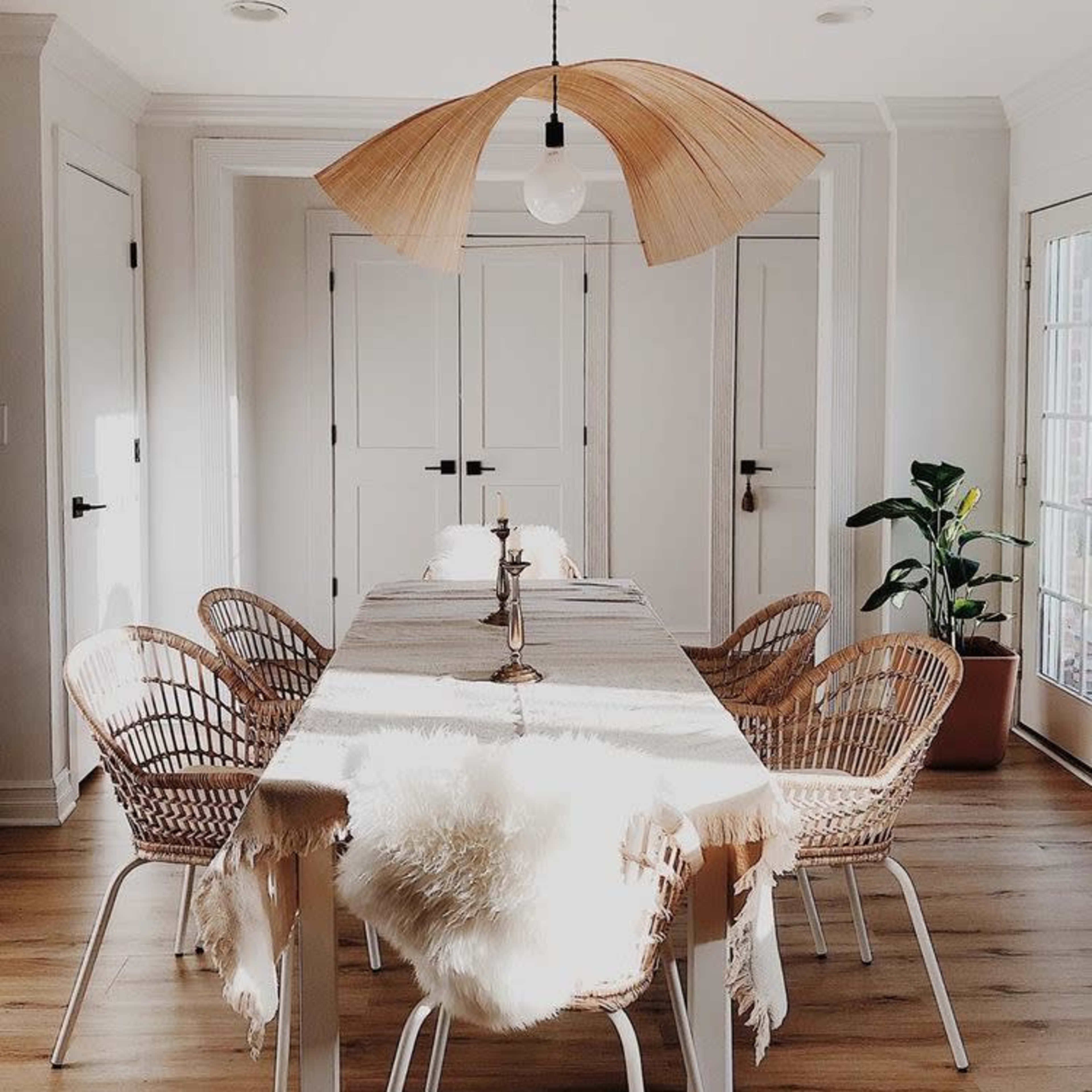 A dining area features a long table surrounded by rattan chairs, with a unique pendant light above and a potted plant in the corner.