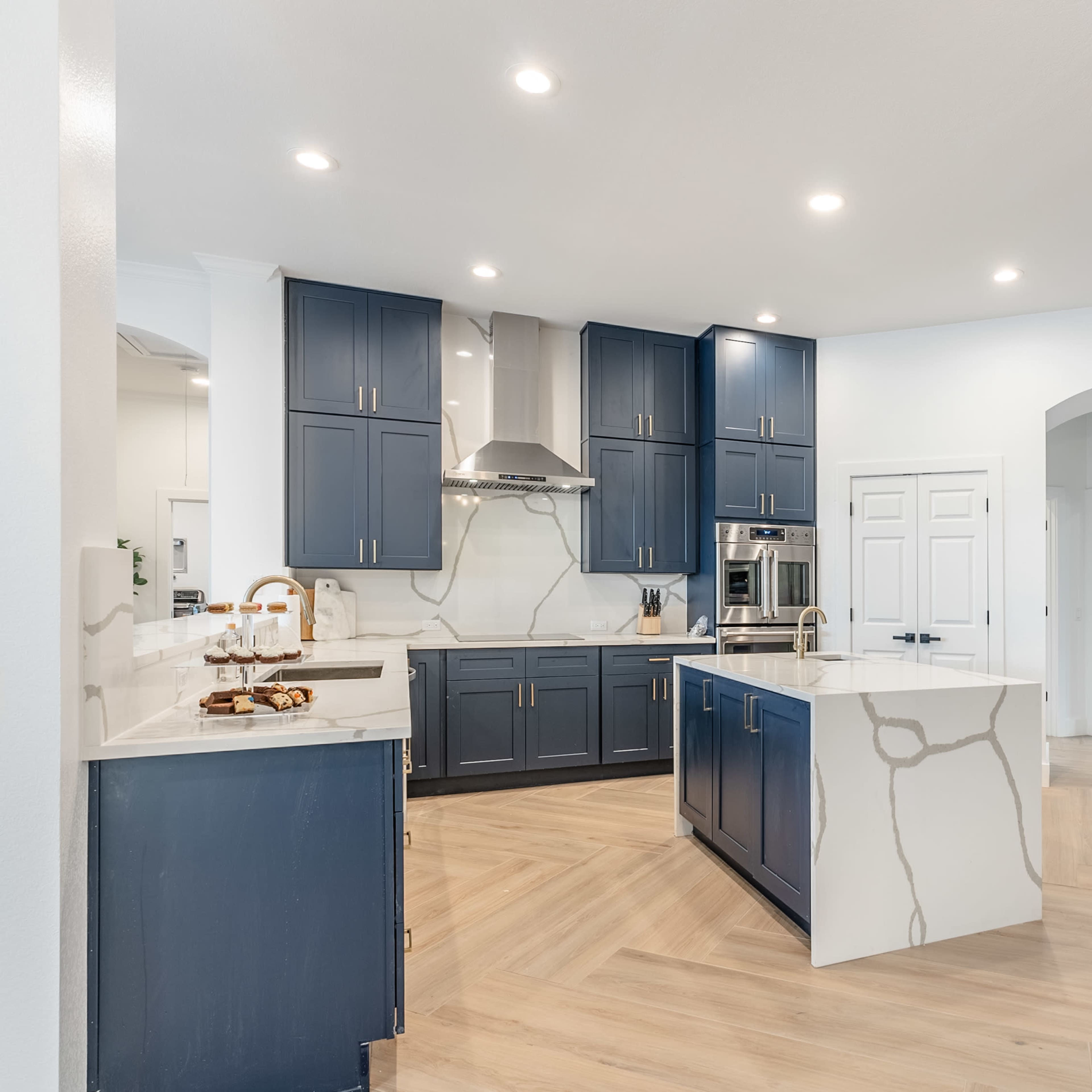 A modern kitchen featuring navy blue cabinets, a large island with a white countertop, and stainless steel appliances.