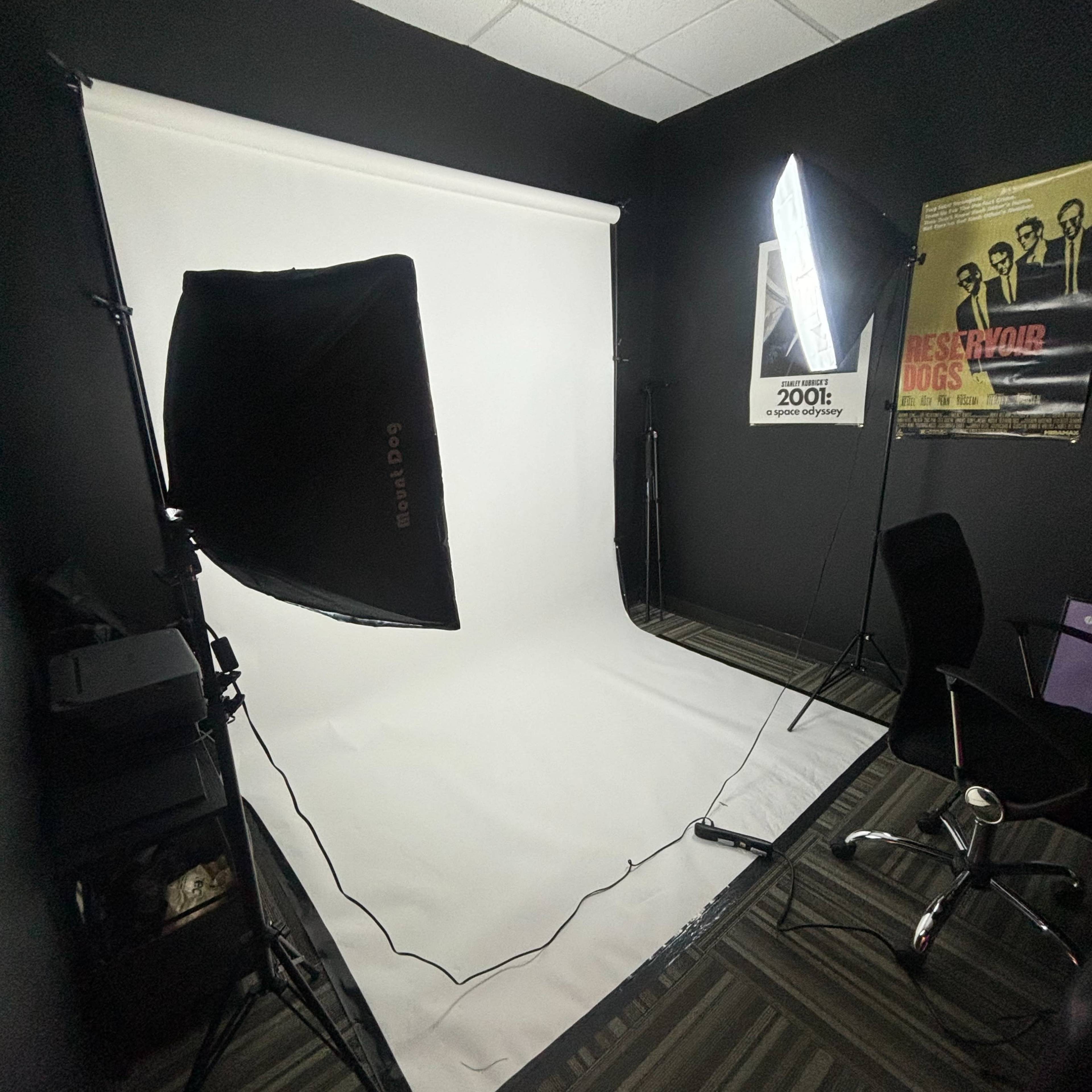A photography studio with a white backdrop, studio lights, and a black office chair in a dimly lit room.