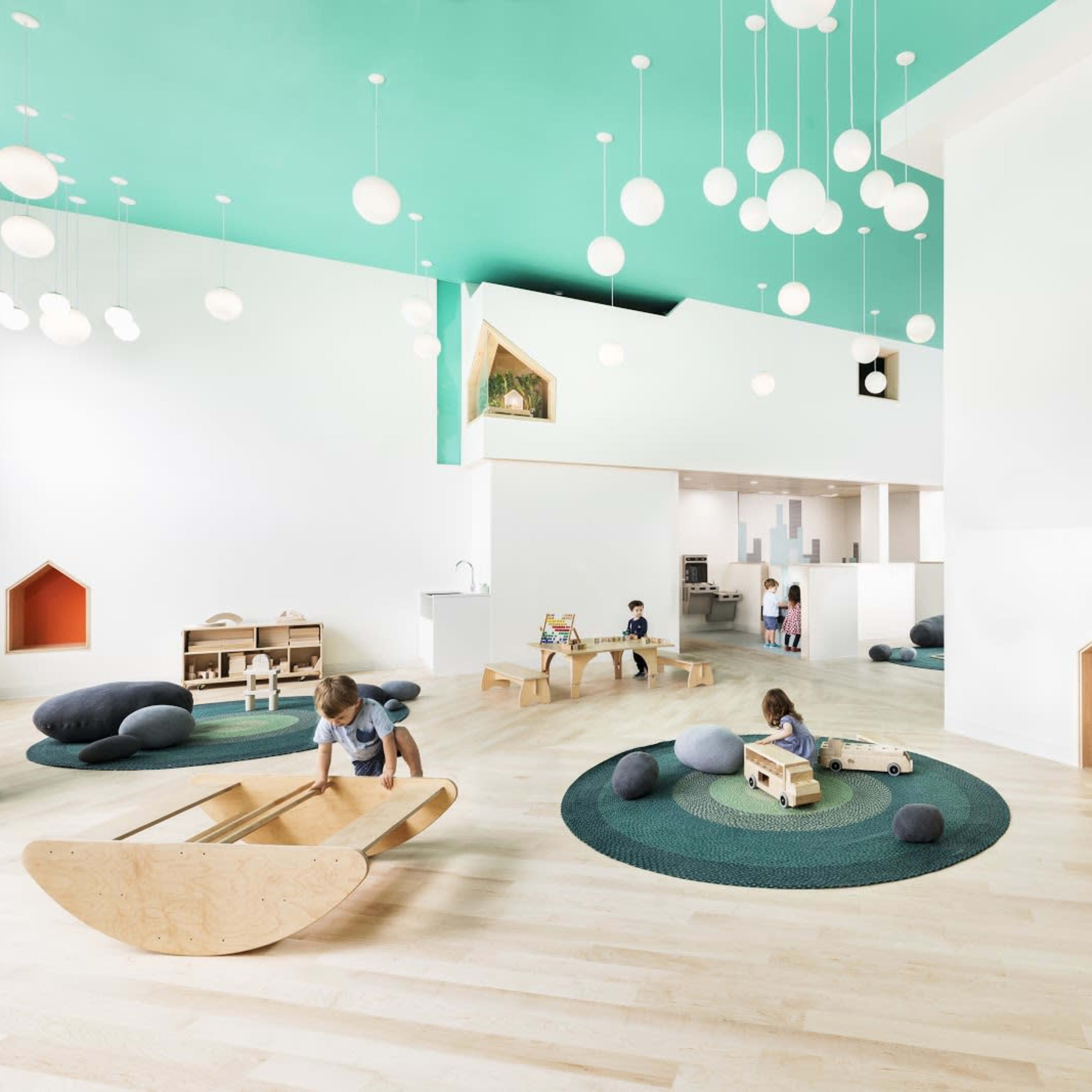 A brightly lit children's play area featuring wooden toys, circular rugs, and whimsical architectural elements.