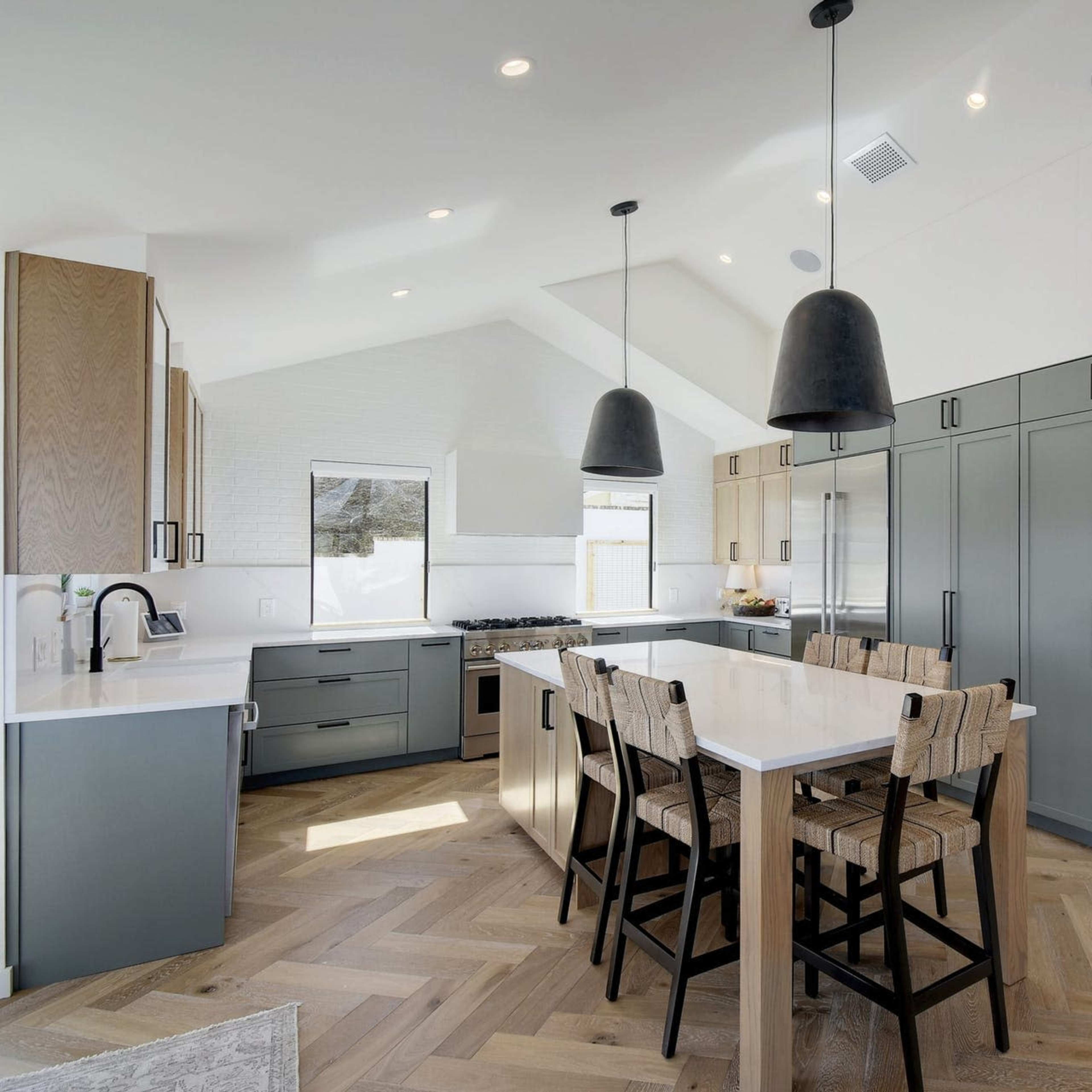 A contemporary kitchen with a large island, wooden bar stools, and a blend of gray and wooden cabinetry.