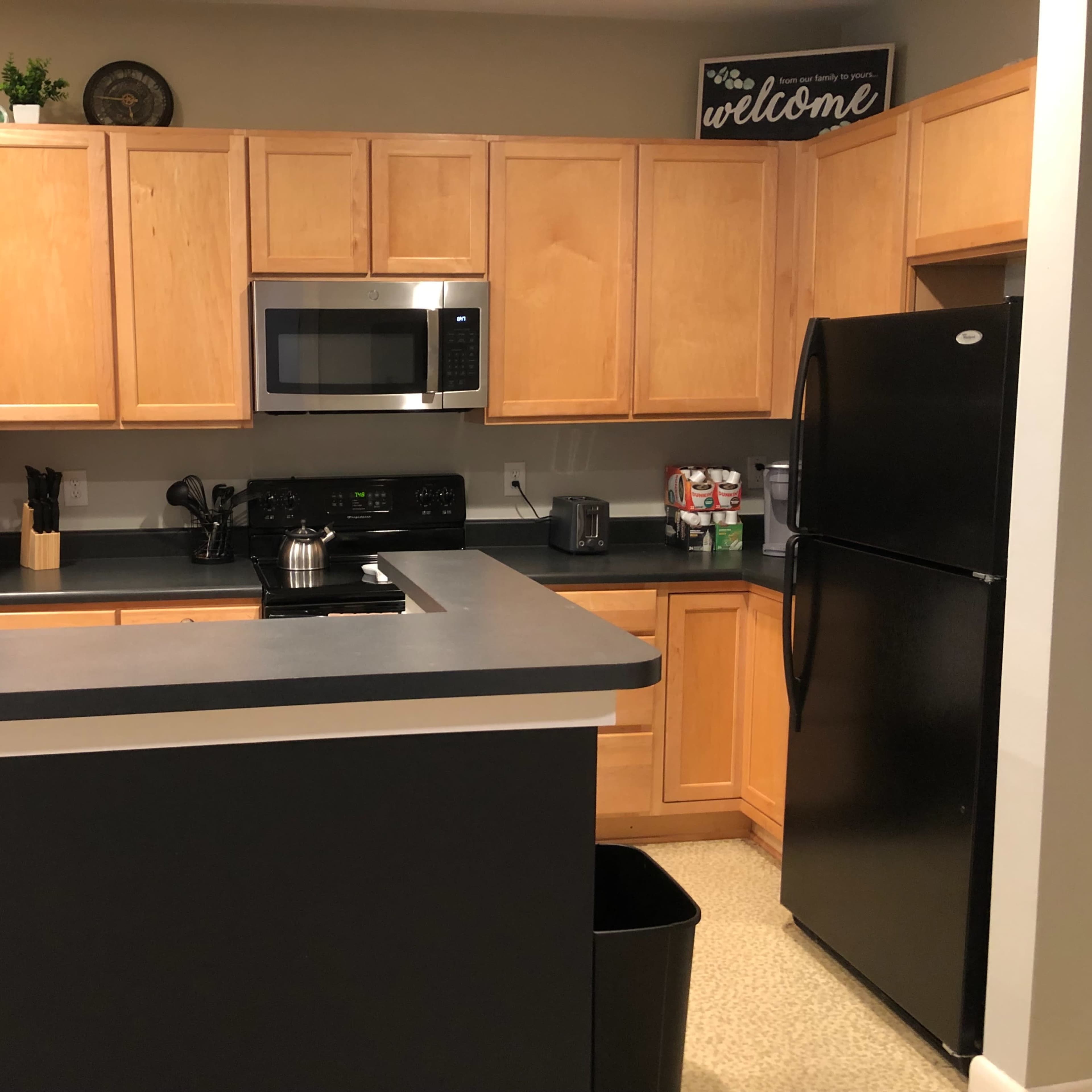 A kitchen with wooden cabinets, black countertops, a microwave, and a black refrigerator.