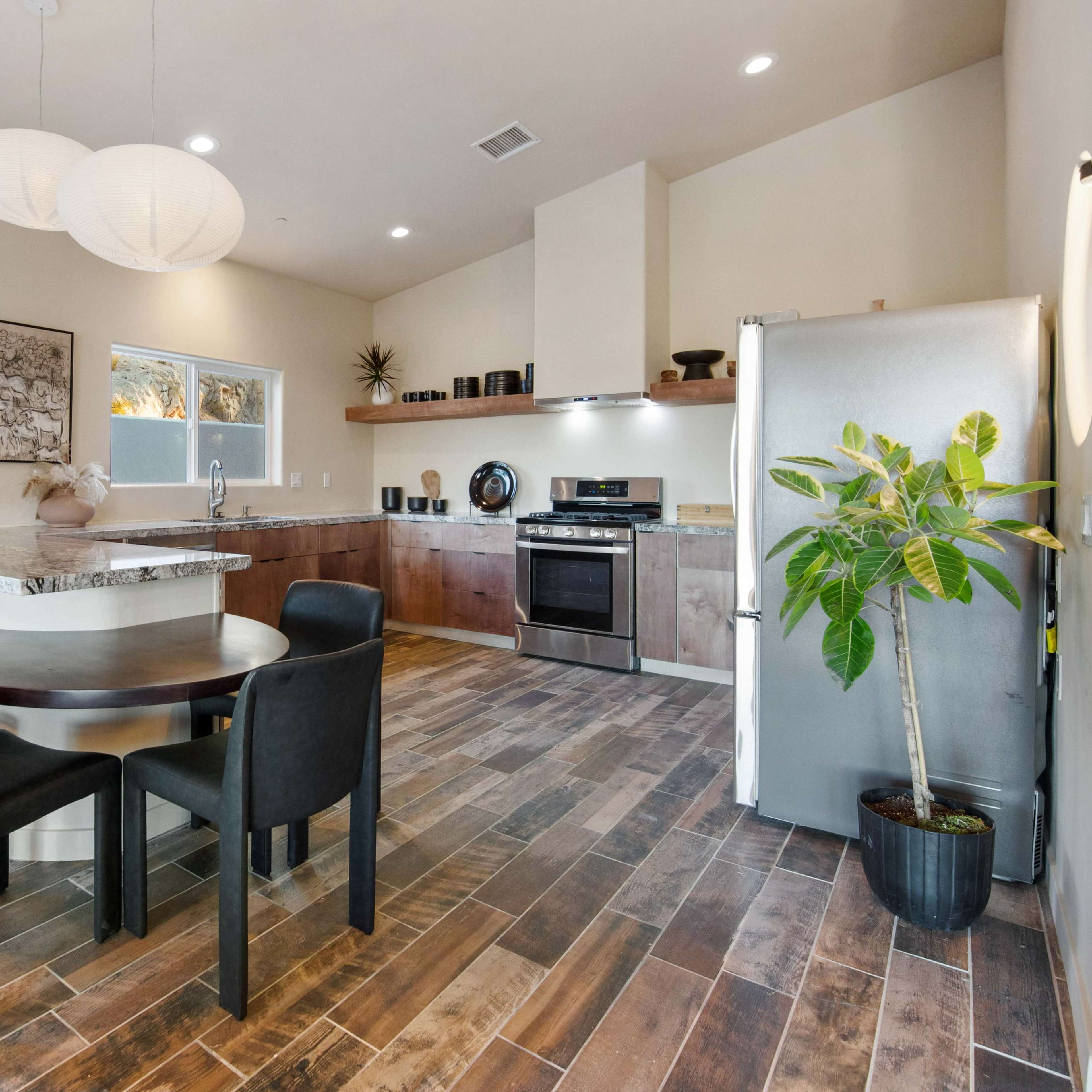 A modern kitchen and dining area features a round table with black chairs, granite countertops, and stainless steel appliances.