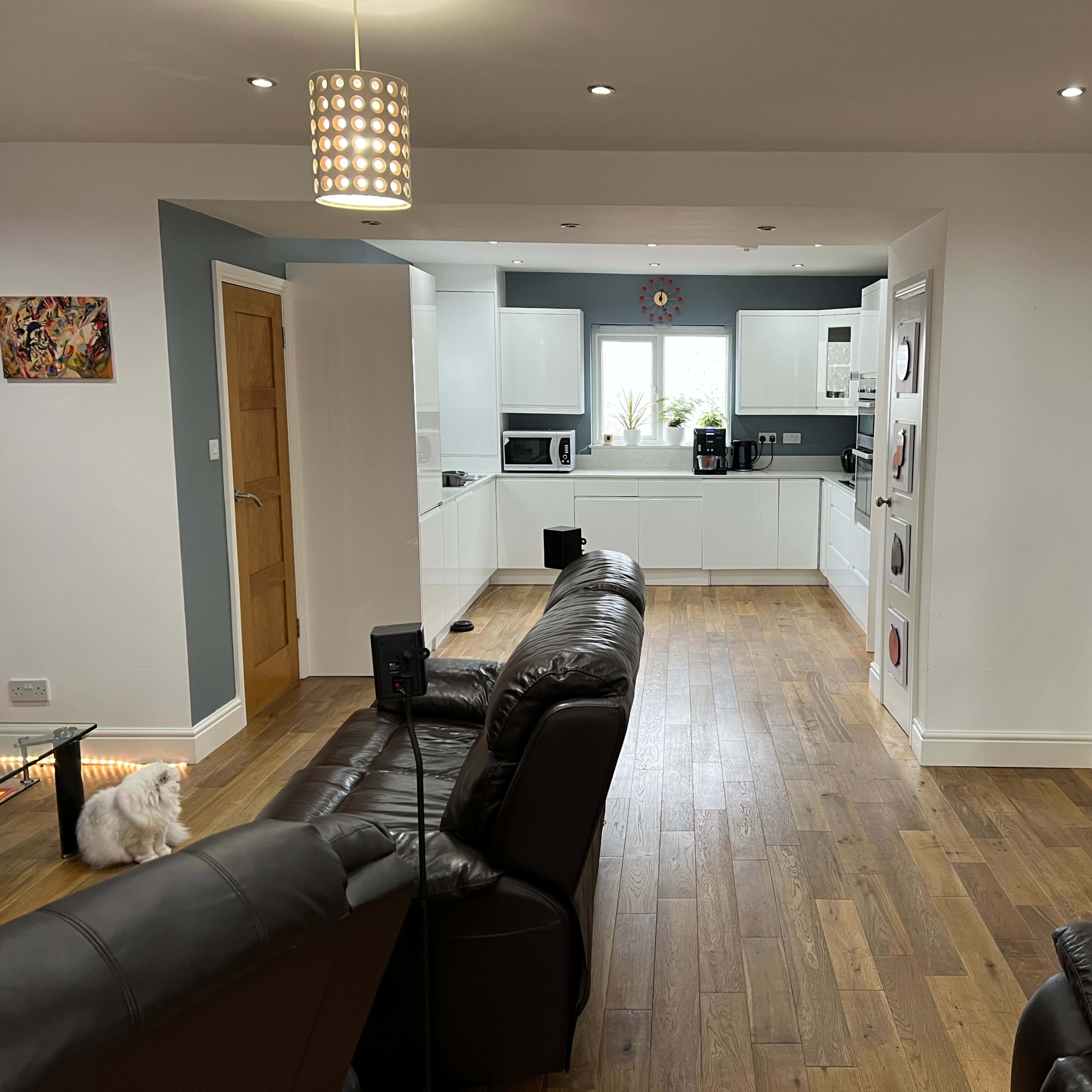 A modern open-plan living area with a kitchen, dining space, and seating area, featuring wooden flooring and light-colored cabinetry.