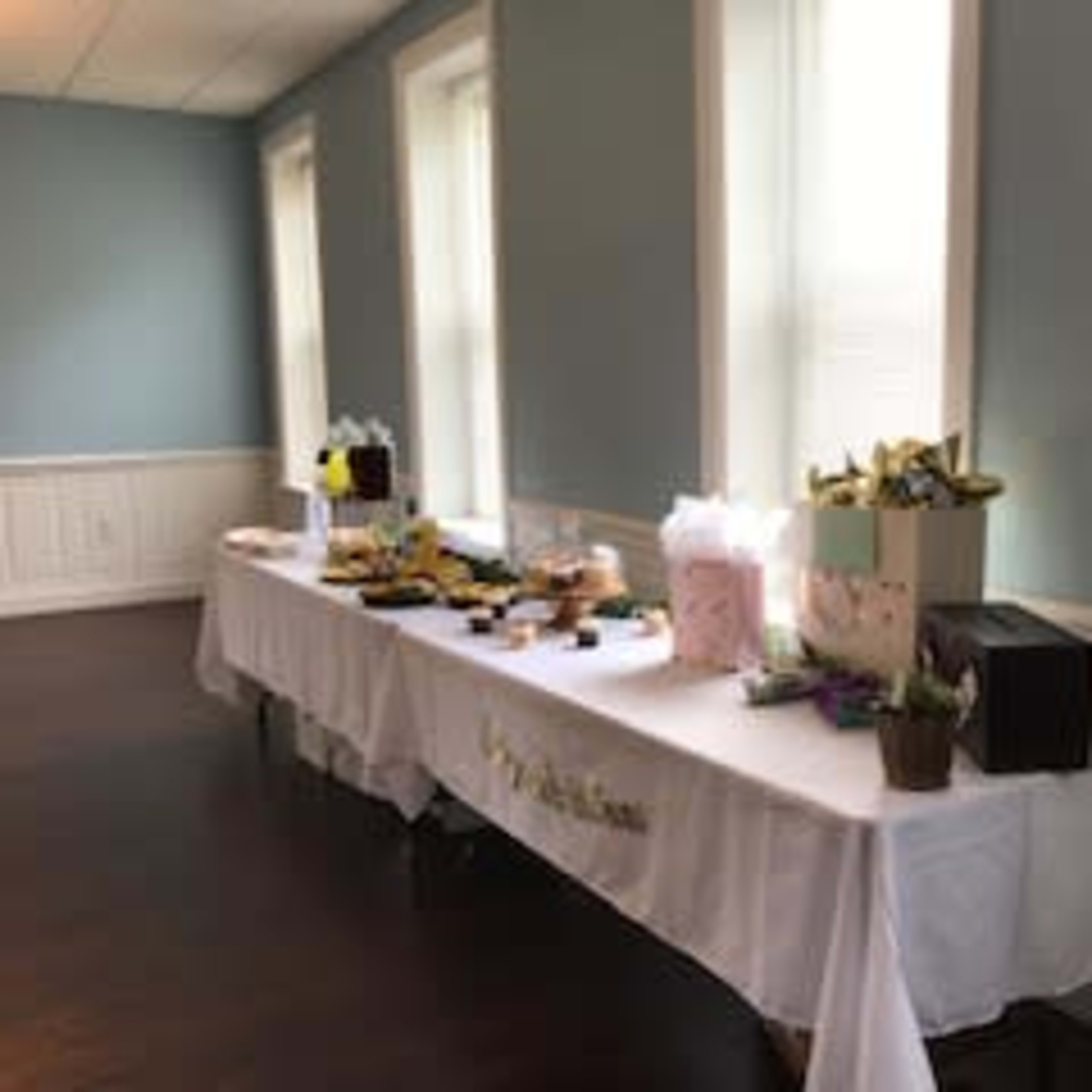 A long table is set up in a room with blue walls, displaying an assortment of food, gifts, and decorative items.