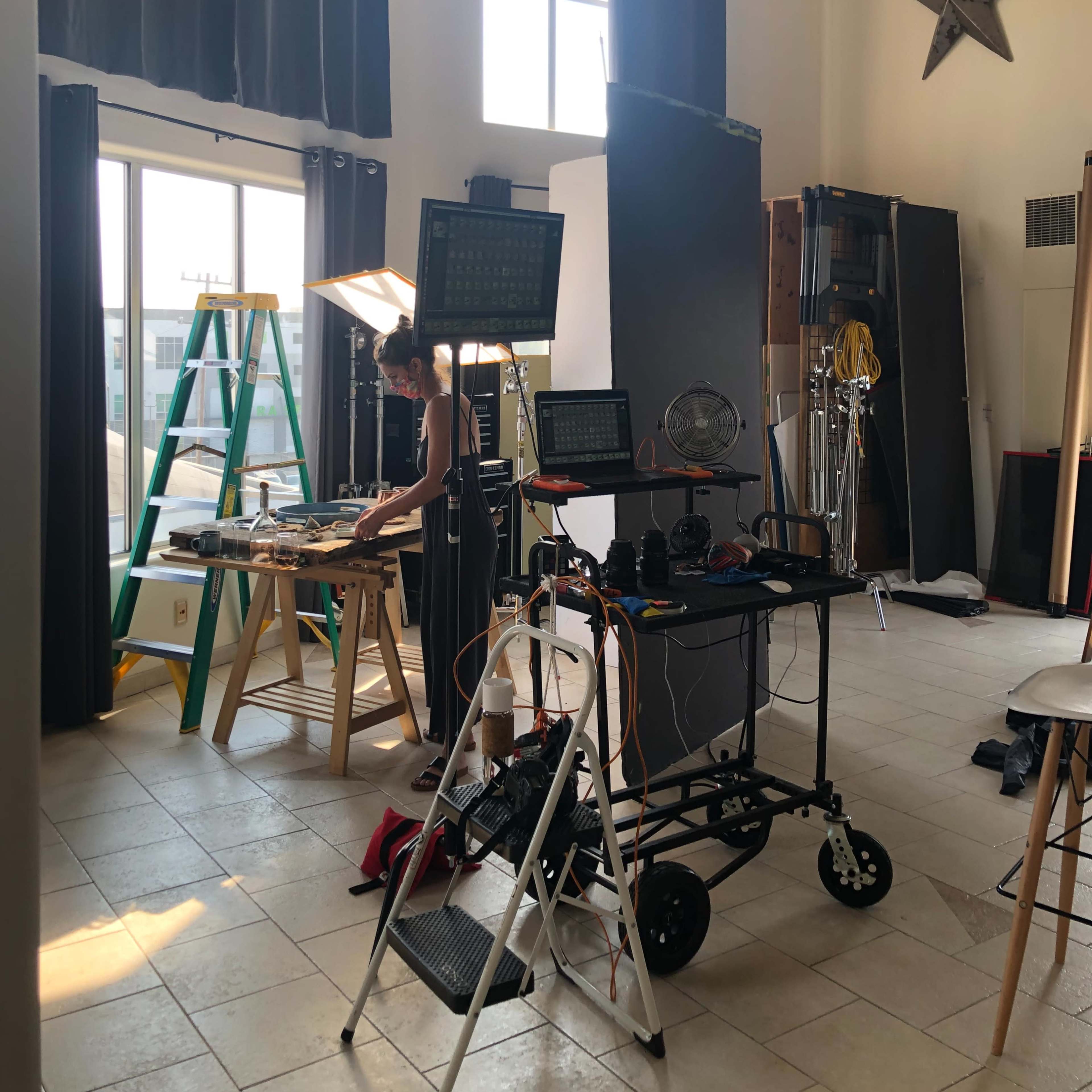 A well-lit studio space features equipment for a photoshoot, including a table with supplies, lights, and a ladder.
