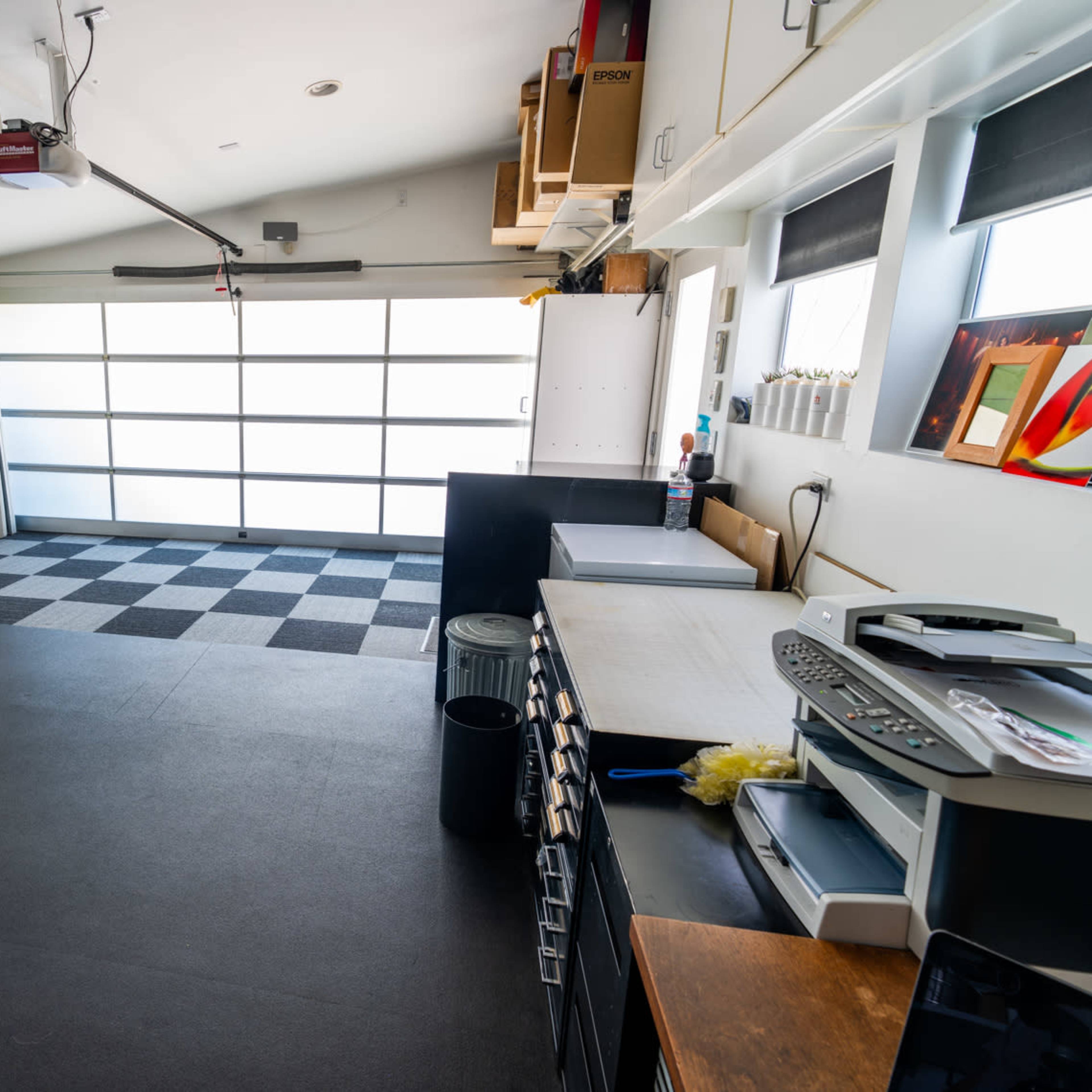 A spacious, organized garage with a checkered floor, a large overhead door, and storage cabinets lining the walls.