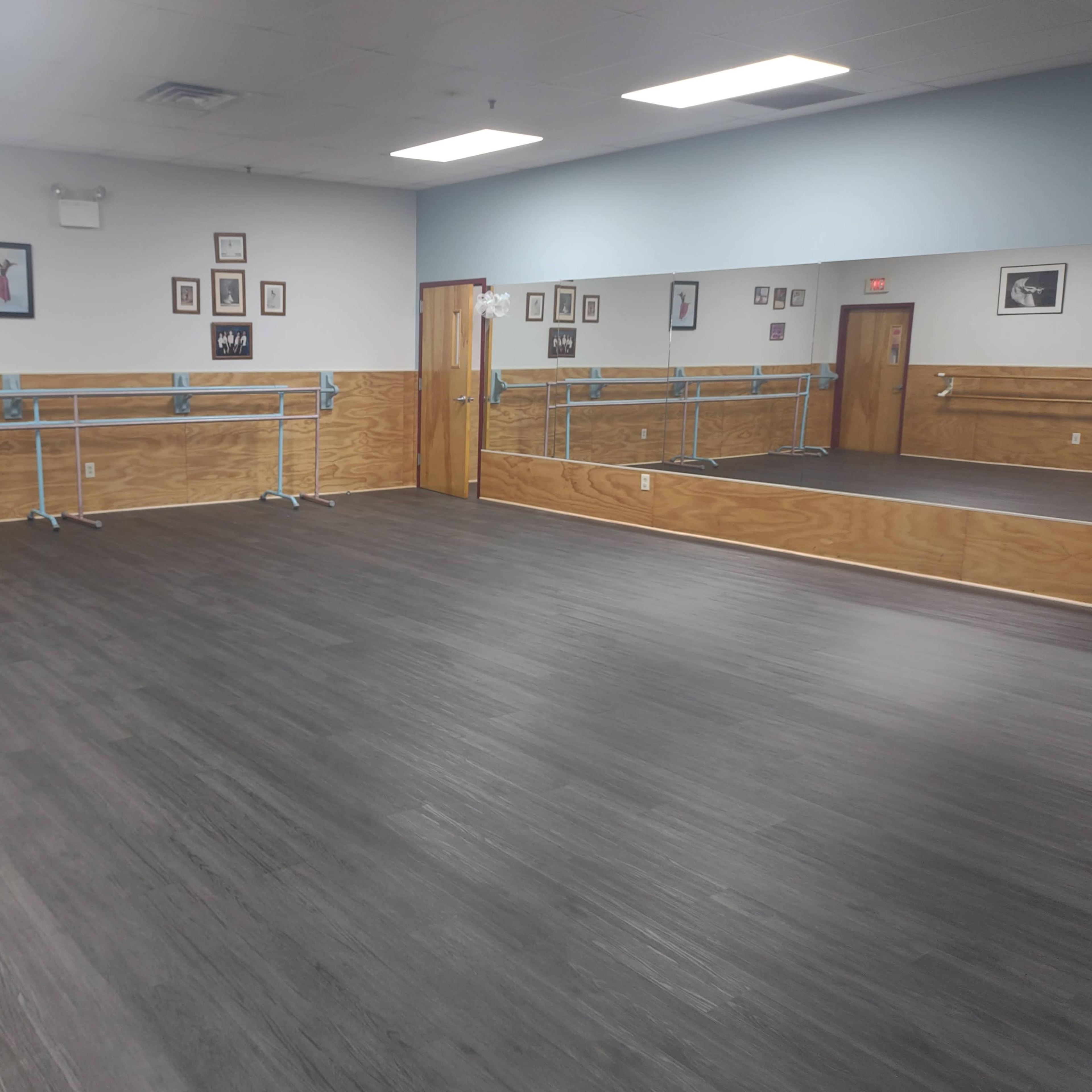 A spacious dance studio with wooden walls, a mirrored wall, and ballet barres along the sides.