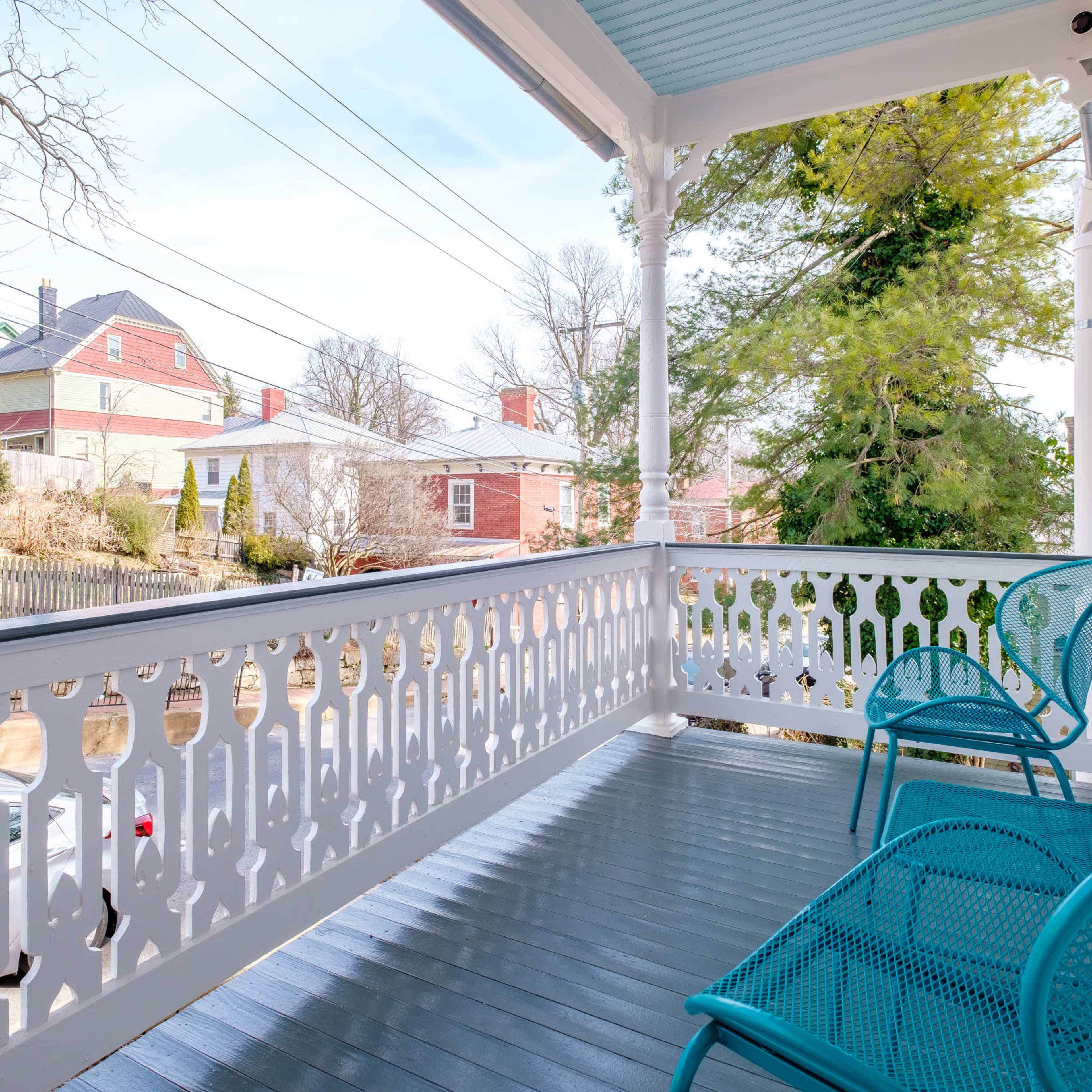 A porch features two blue chairs overlooking a neighborhood with houses and trees in the background.