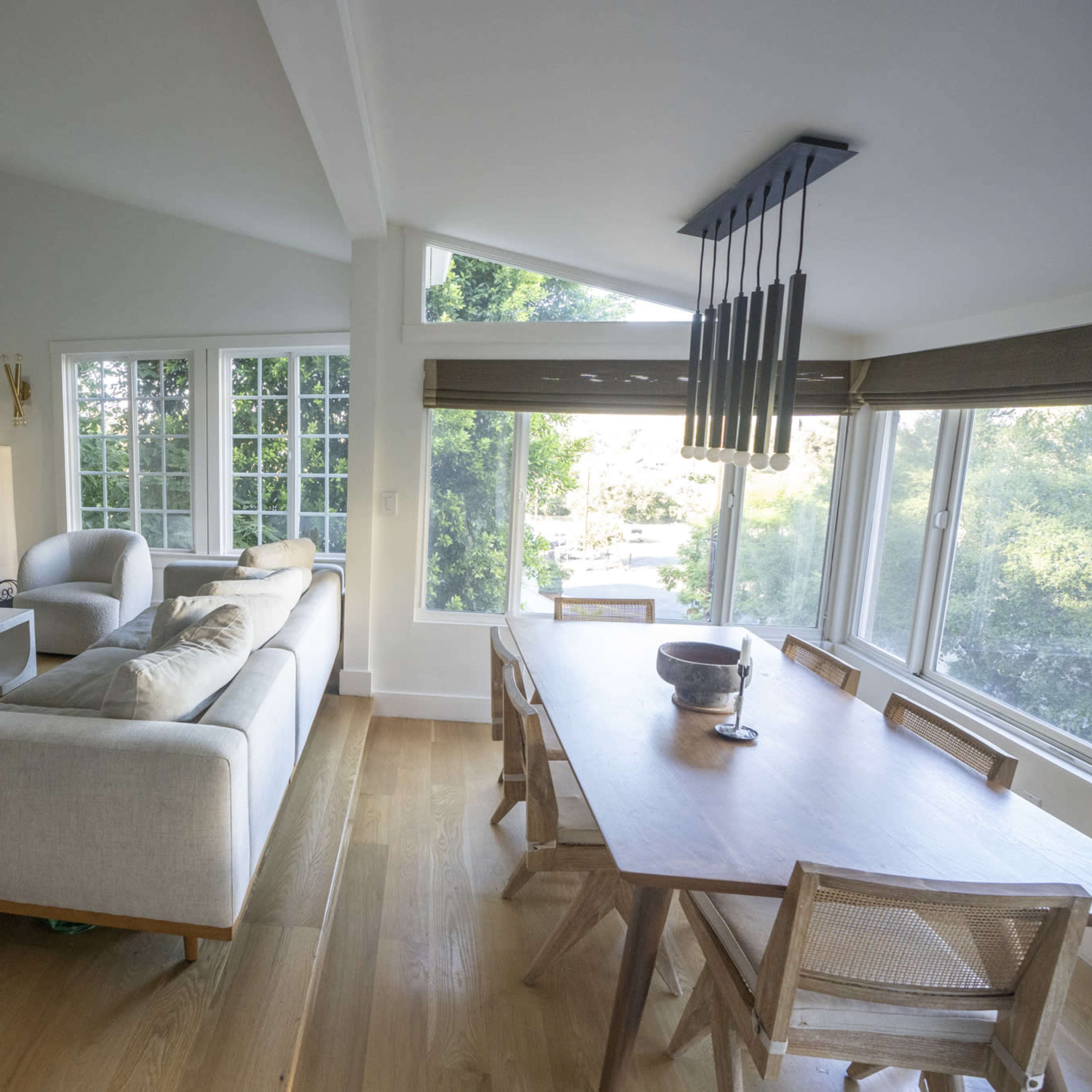 A modern living room features a large sectional sofa, a dining table, and expansive windows overlooking a garden.
