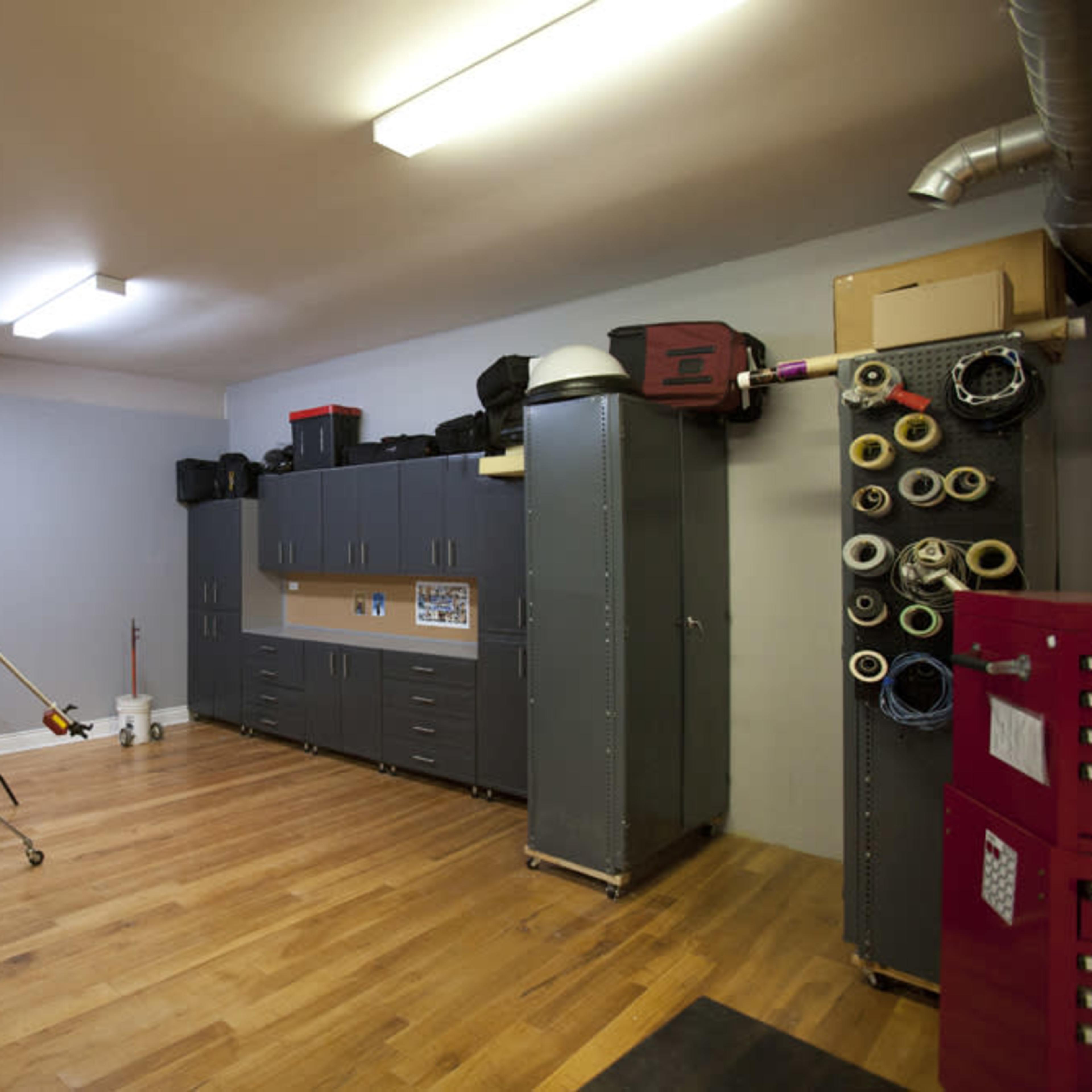 A spacious garage with wooden flooring, storage cabinets, a whiteboard, and photography equipment set up for a shoot.