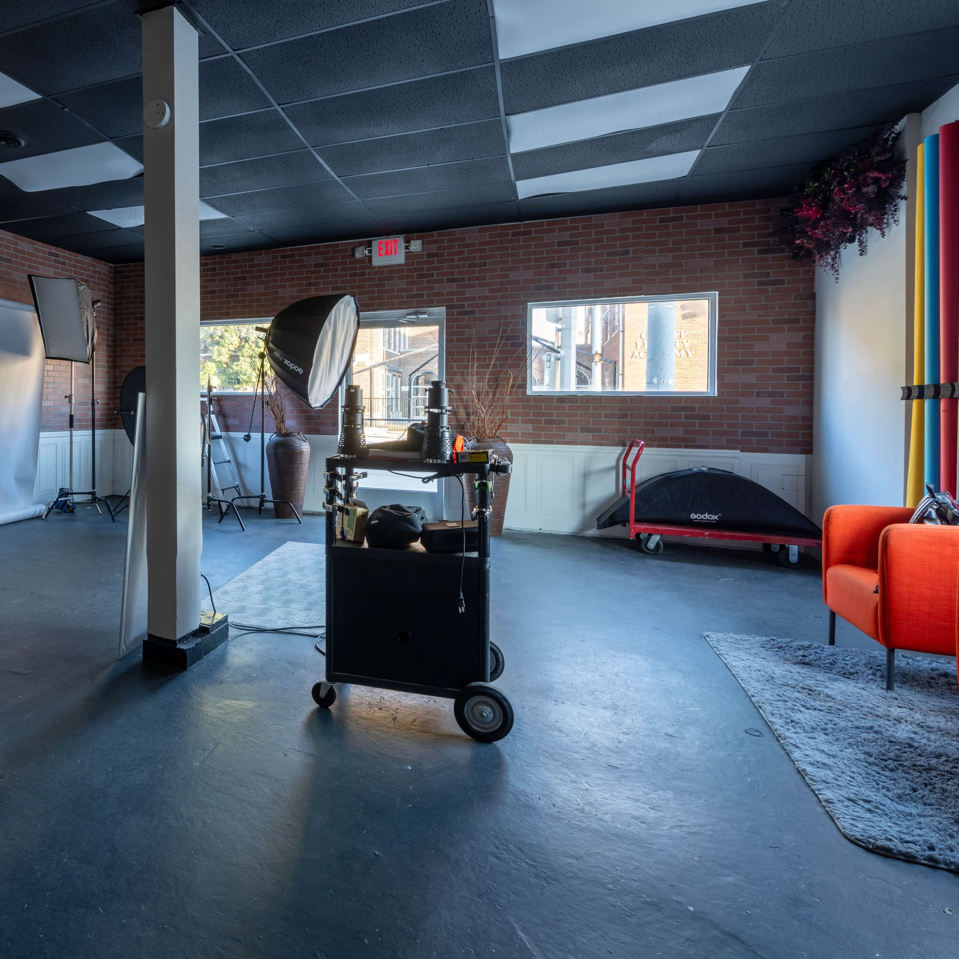 A spacious photography studio with soft lighting equipment, a backdrop stand, and colorful decorations against brick walls.