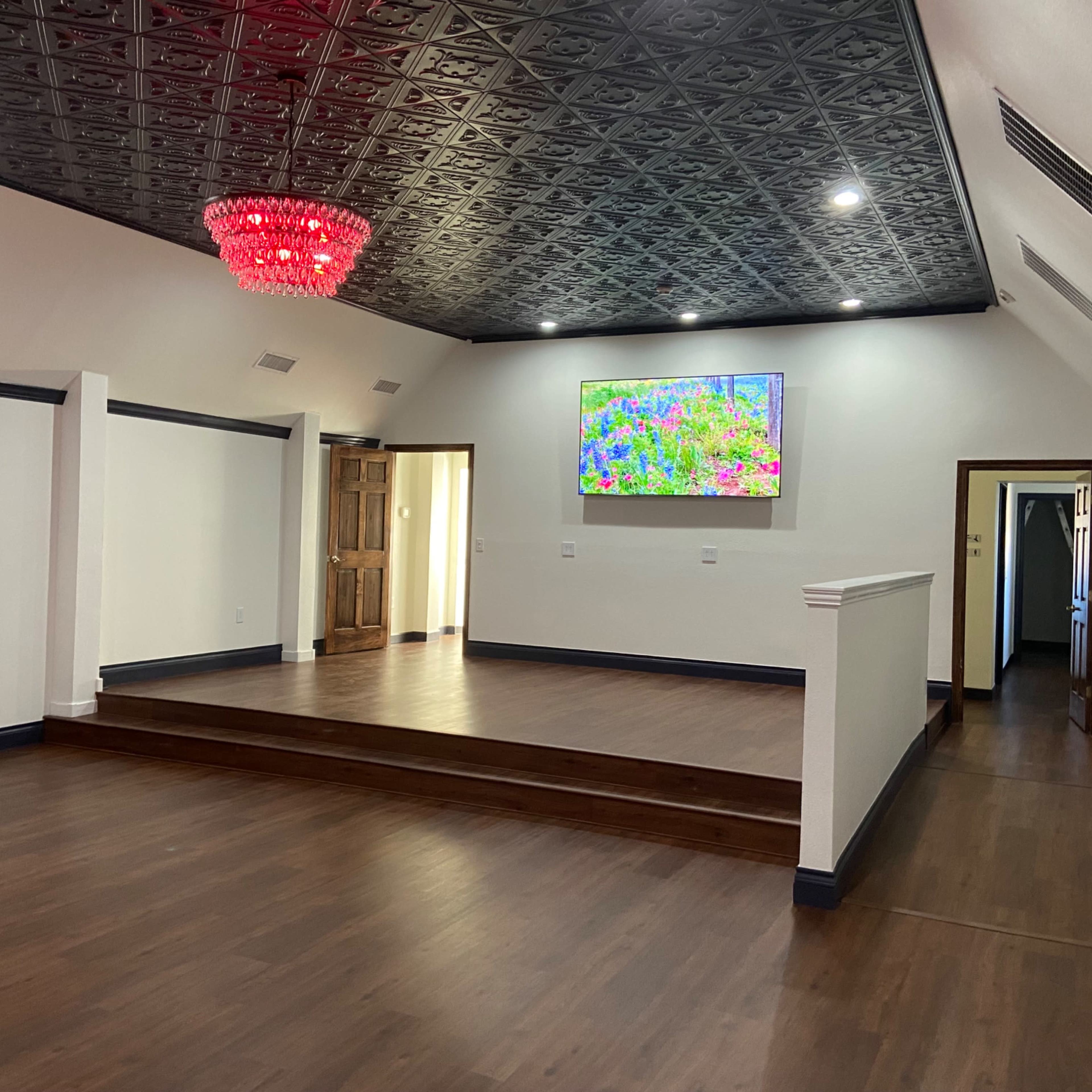 A spacious room with a hardwood floor, a raised platform at one end, and a large screen displaying colorful artwork on the wall.
