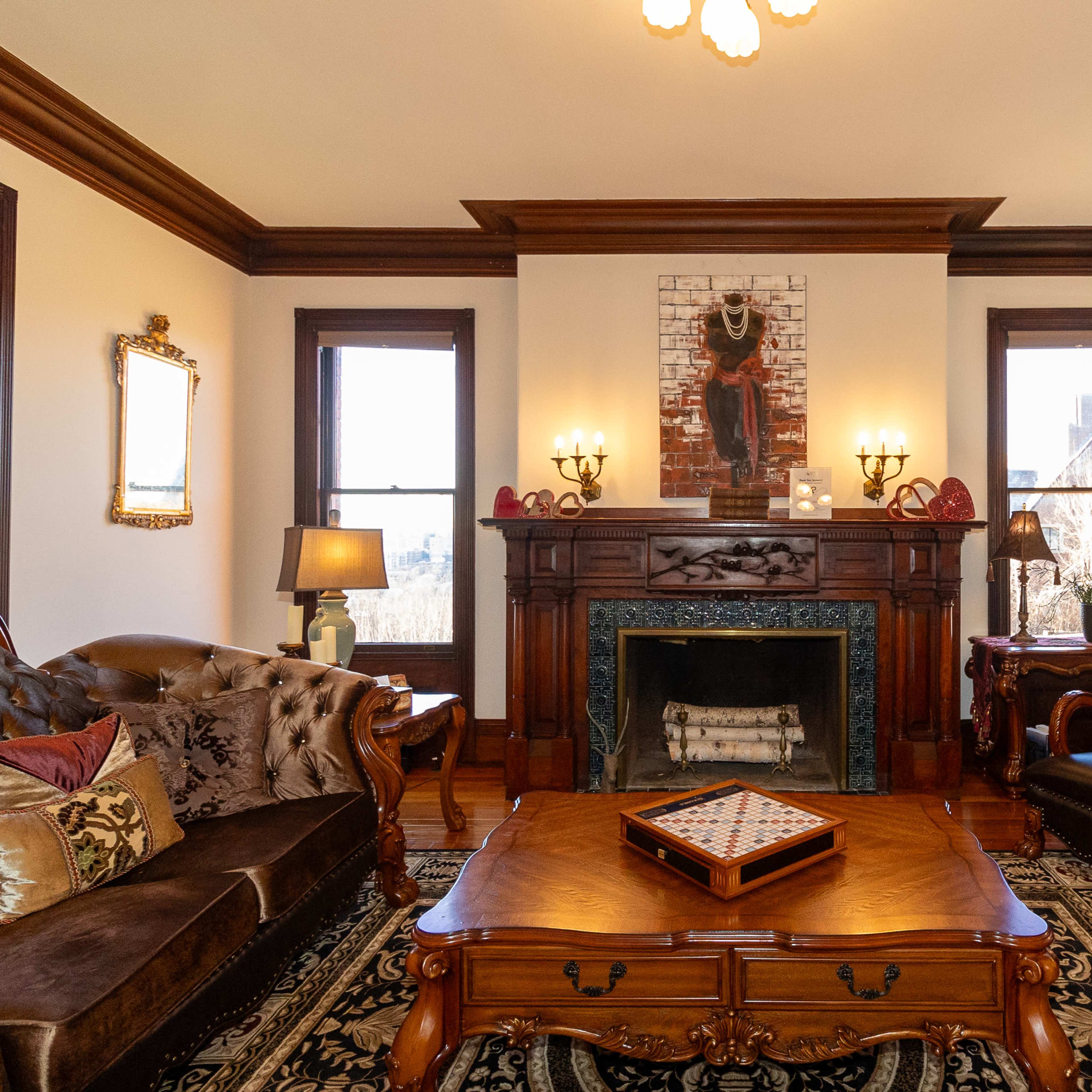 The living room features ornate wooden furniture, a decorative fireplace, and two windows illuminating the space.