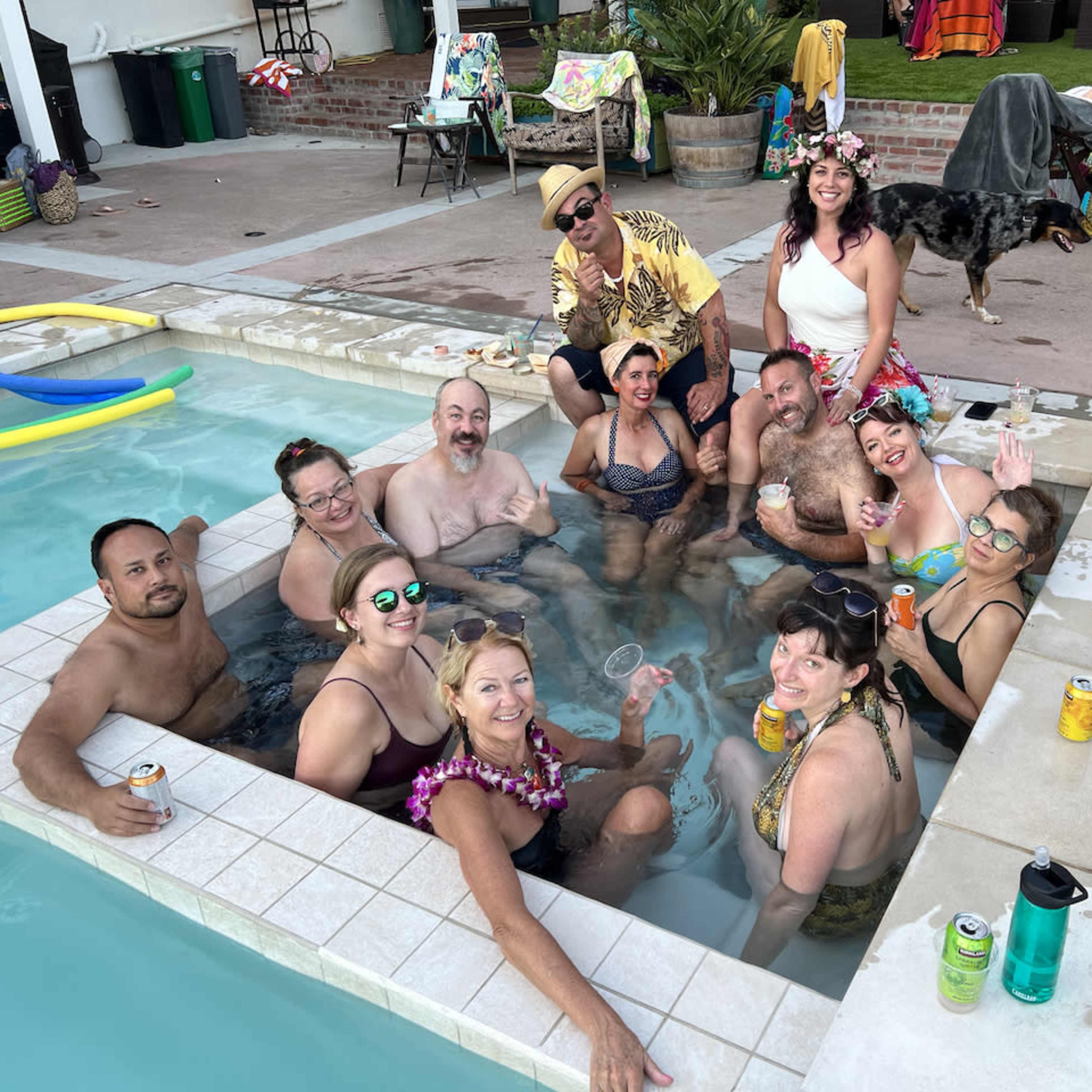 A group of people is gathered in a hot tub at a poolside party, enjoying drinks and socializing.