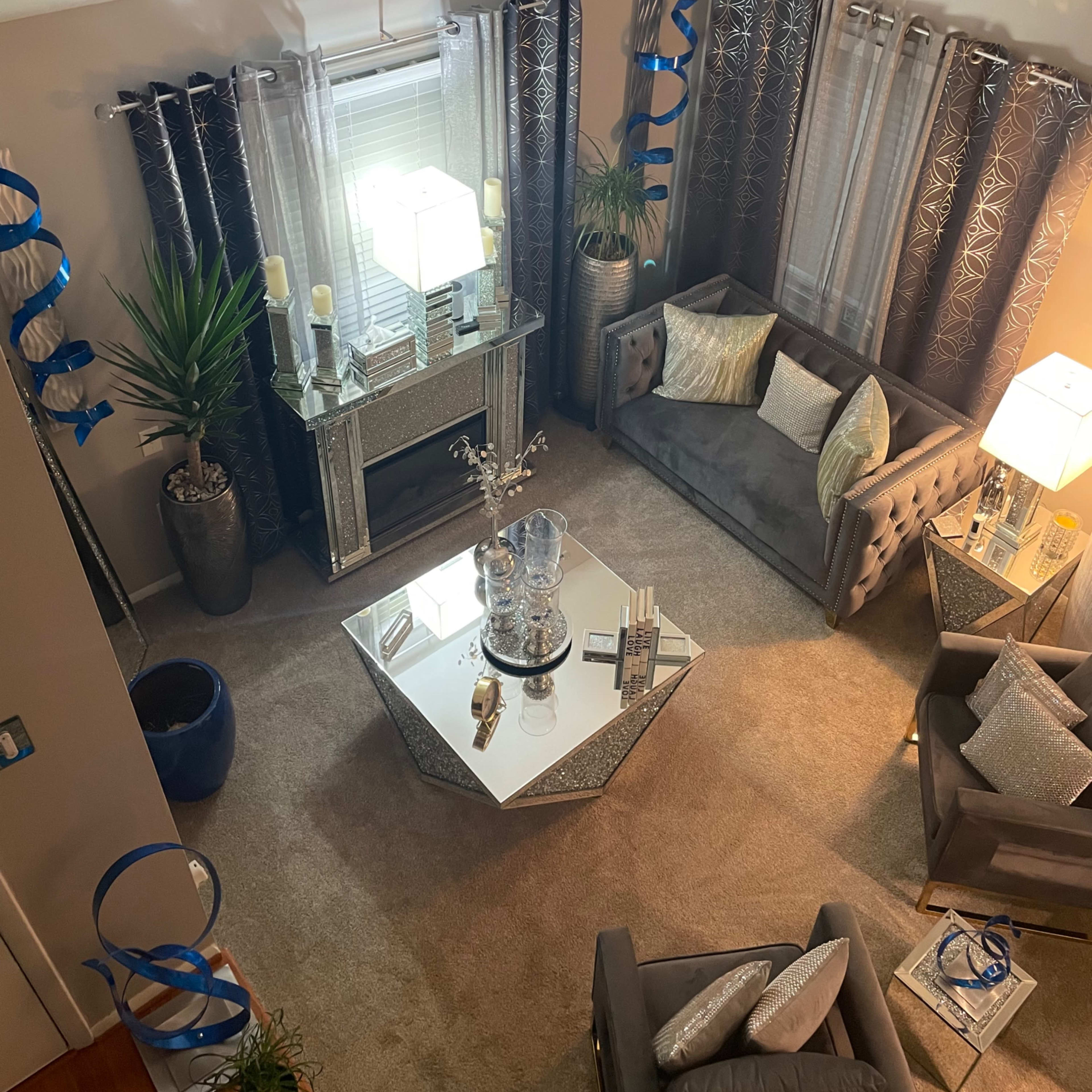 A modern living room with gray furniture, decorative plants, and shimmering light fixtures while blue streamers hang along the walls.