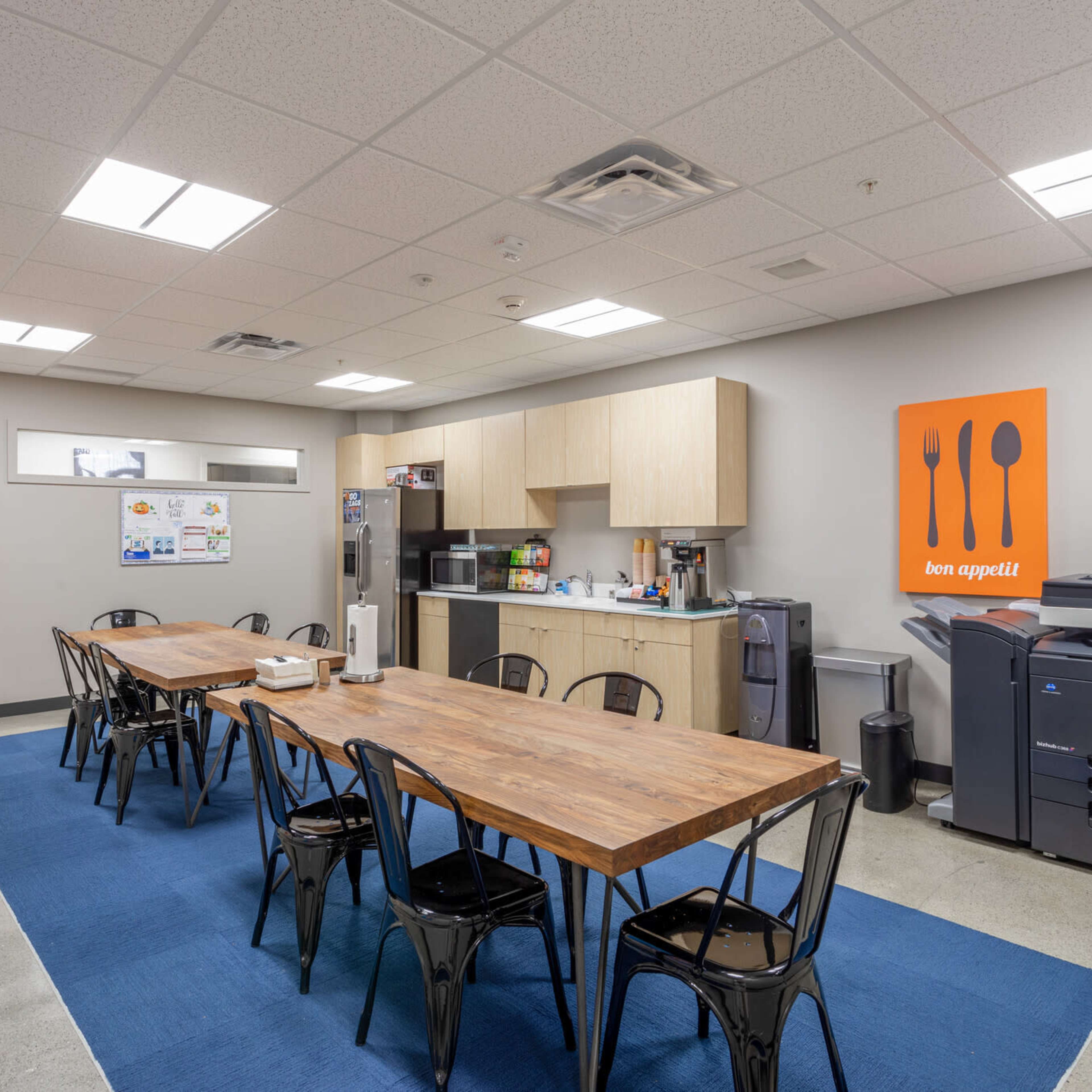 A kitchen and dining area with a long wooden table, black chairs, cabinetry, and various kitchen appliances.