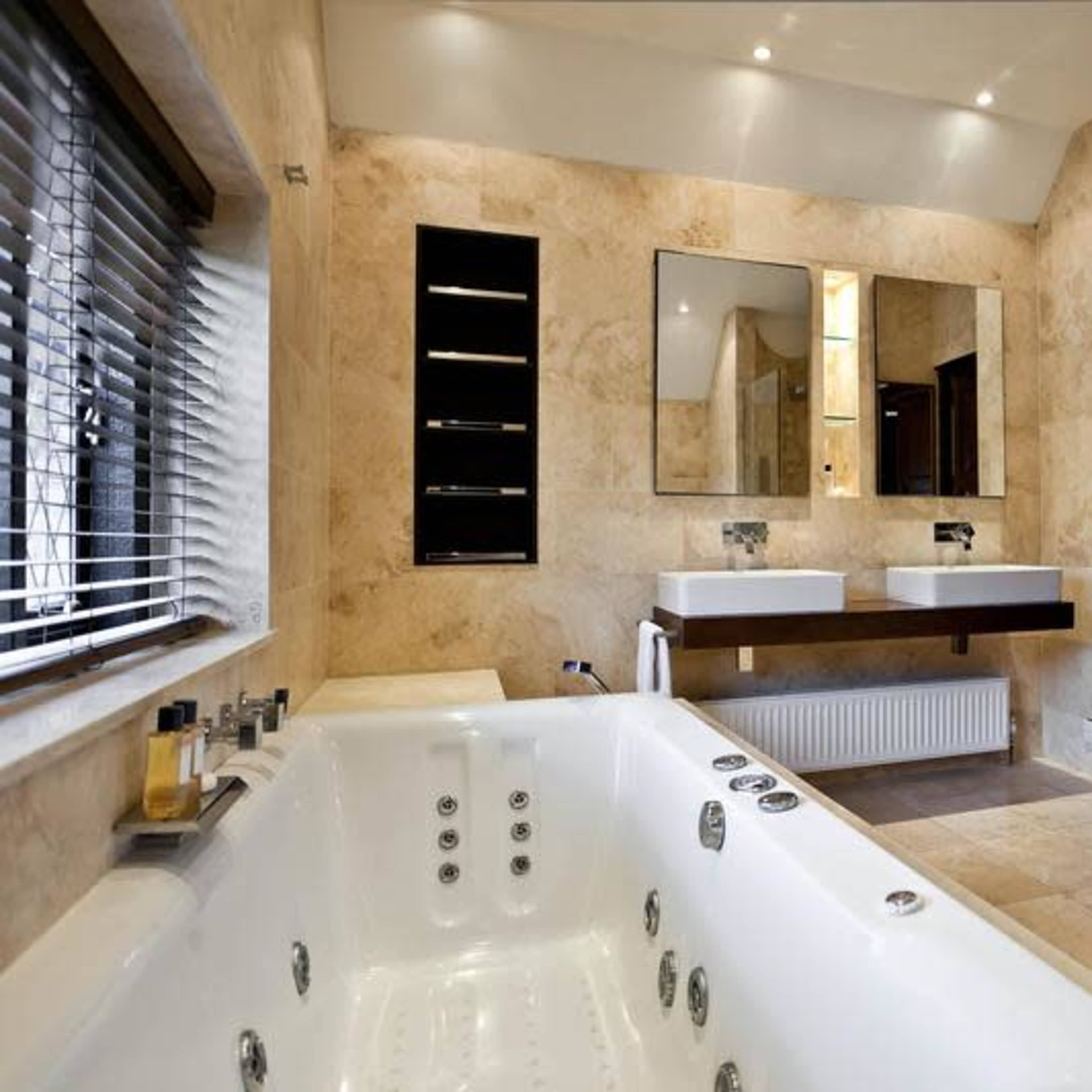 A modern bathroom featuring a whirlpool tub, dual sinks, and a glass shower stall, all with stone finishes.