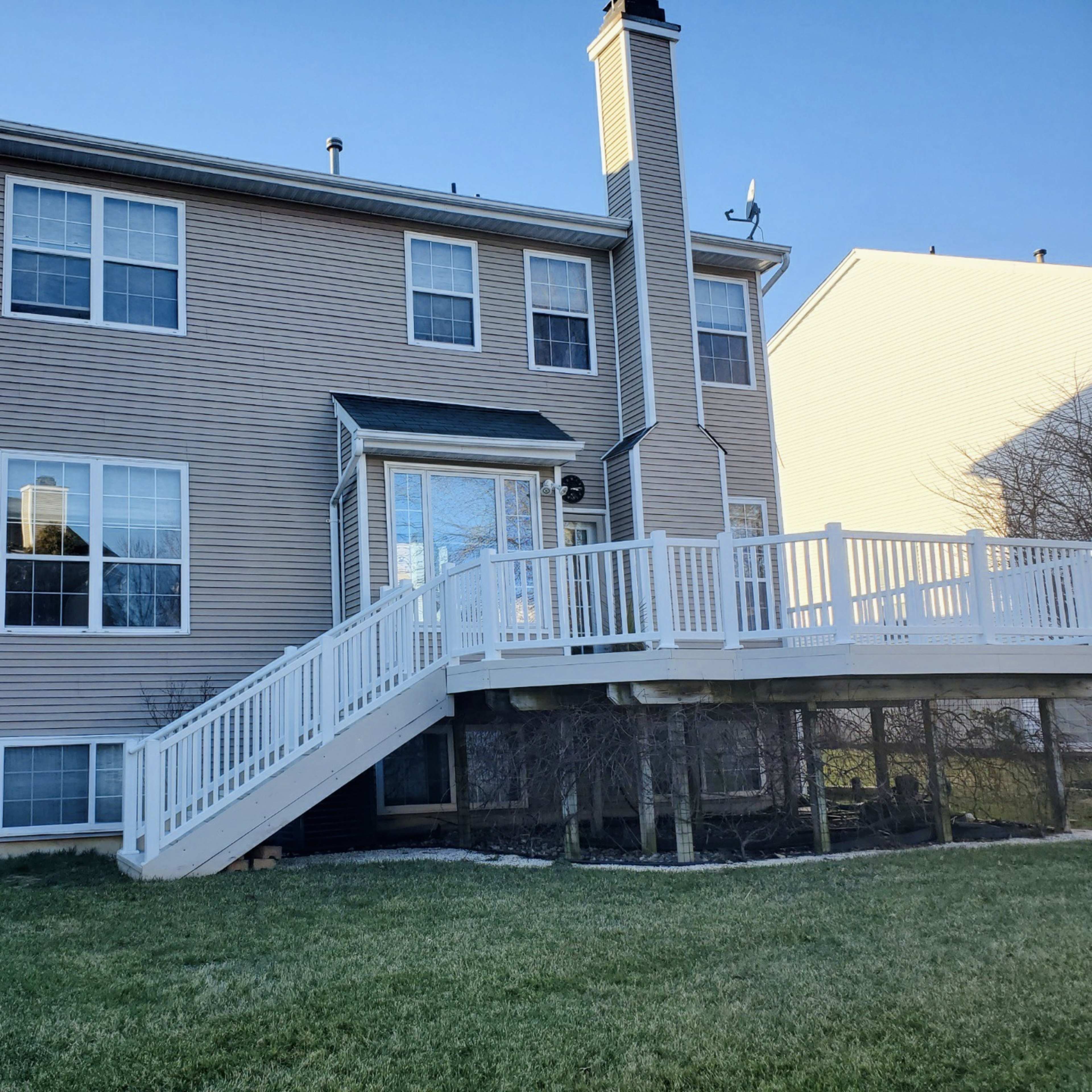 A three-story house with beige siding and a white deck on the back.