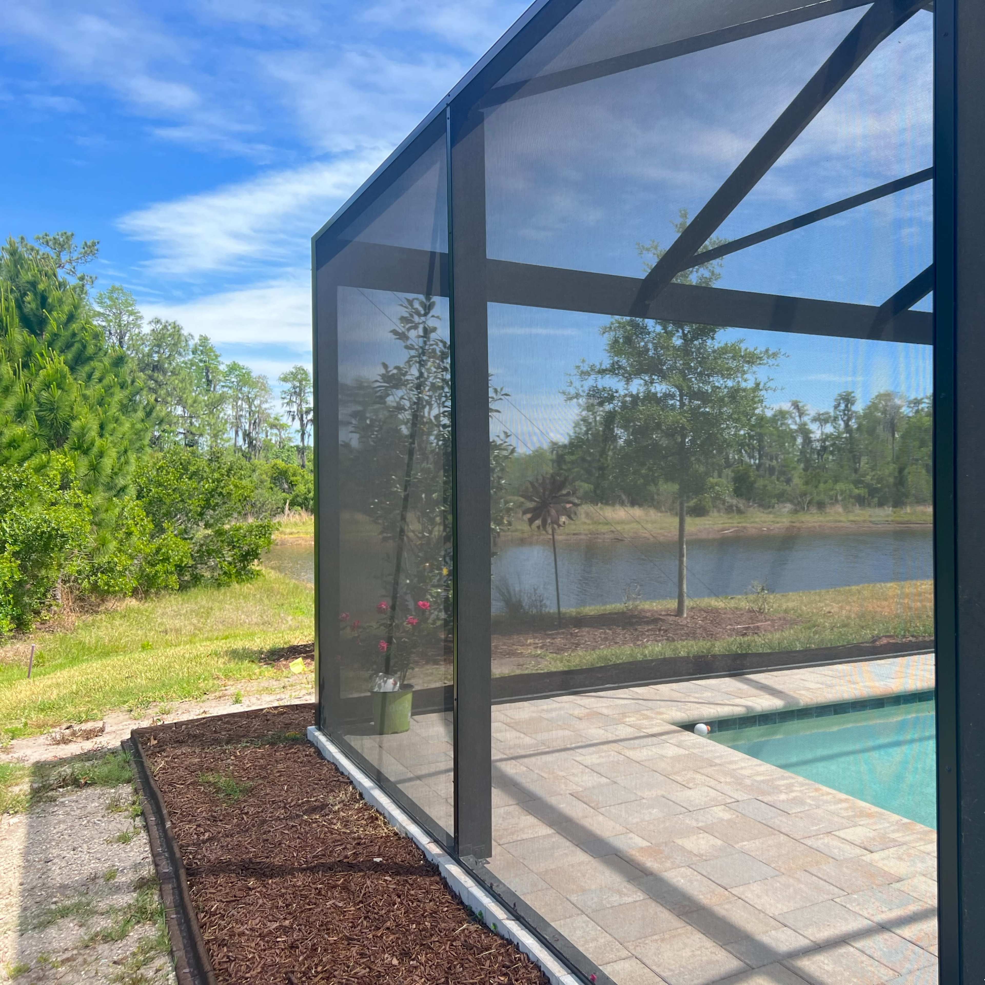 A screened enclosure surrounds a pool with a view of a lake and greenery in the background.