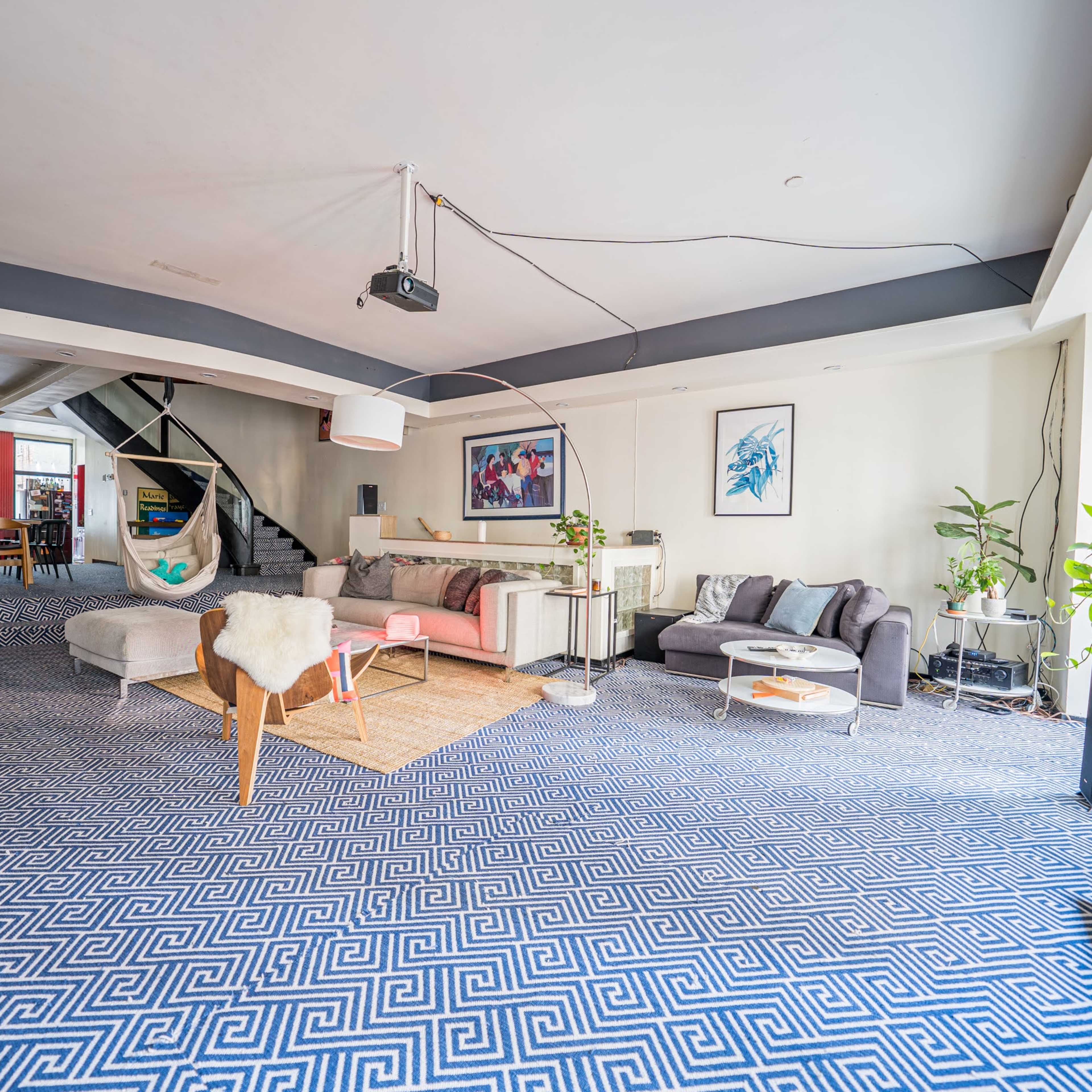 A spacious living area with modern furniture, a large patterned rug, and a staircase in the background.