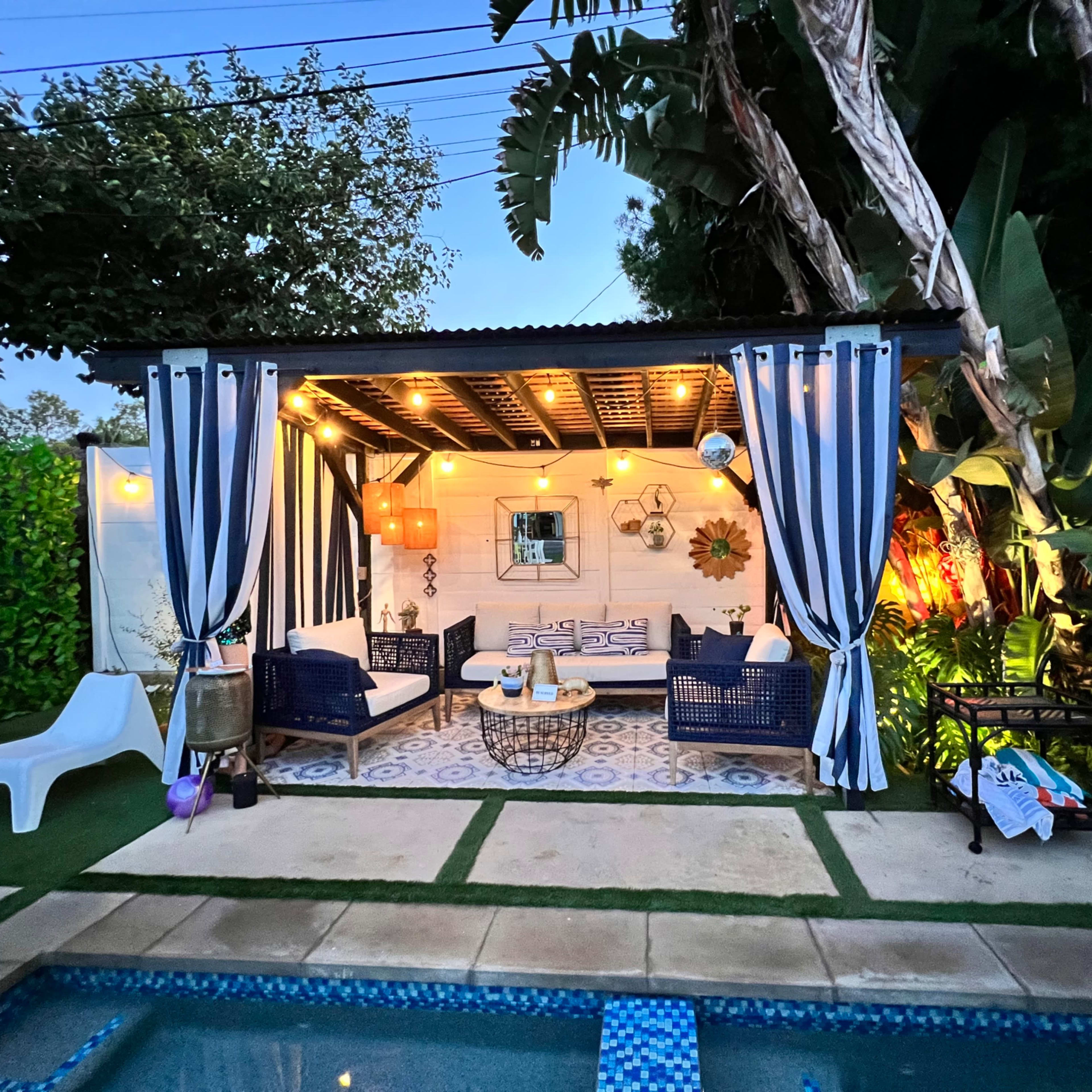 A covered outdoor lounge area with seating and decorative lights is adjacent to a swimming pool.