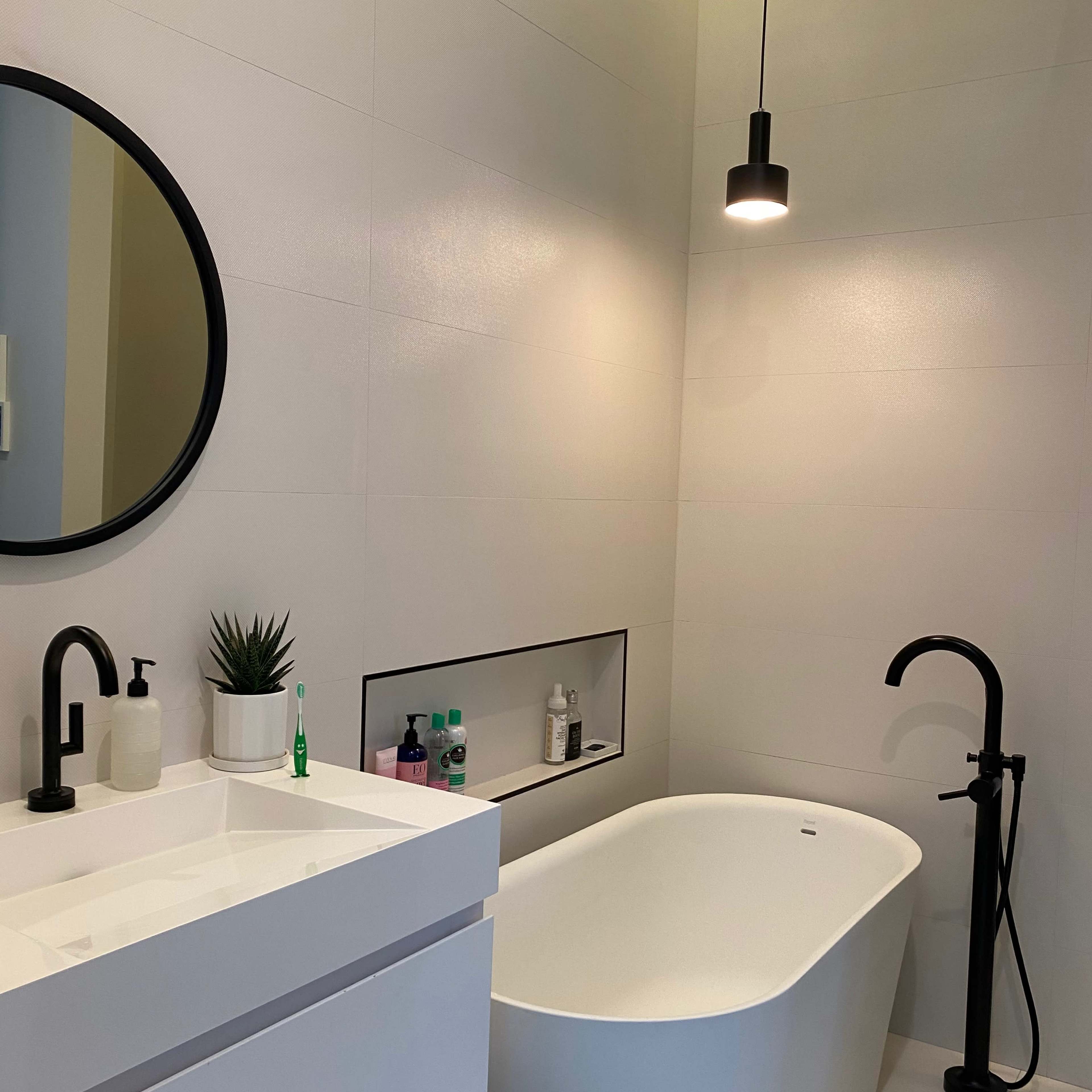 A modern bathroom featuring a freestanding bathtub, a round mirror, and minimalistic sink cabinetry under a pendant light.
