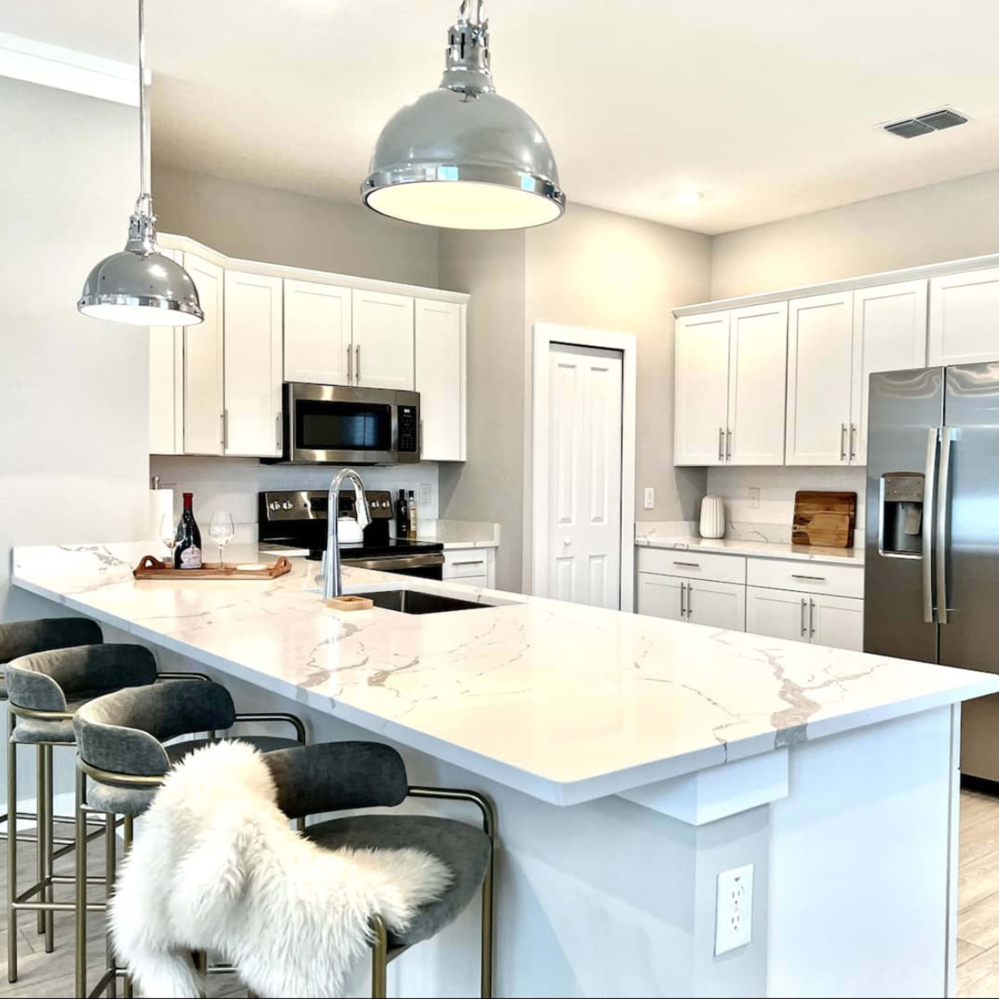 A modern kitchen features white cabinetry, stainless steel appliances, and a large marble-topped island with bar stools.