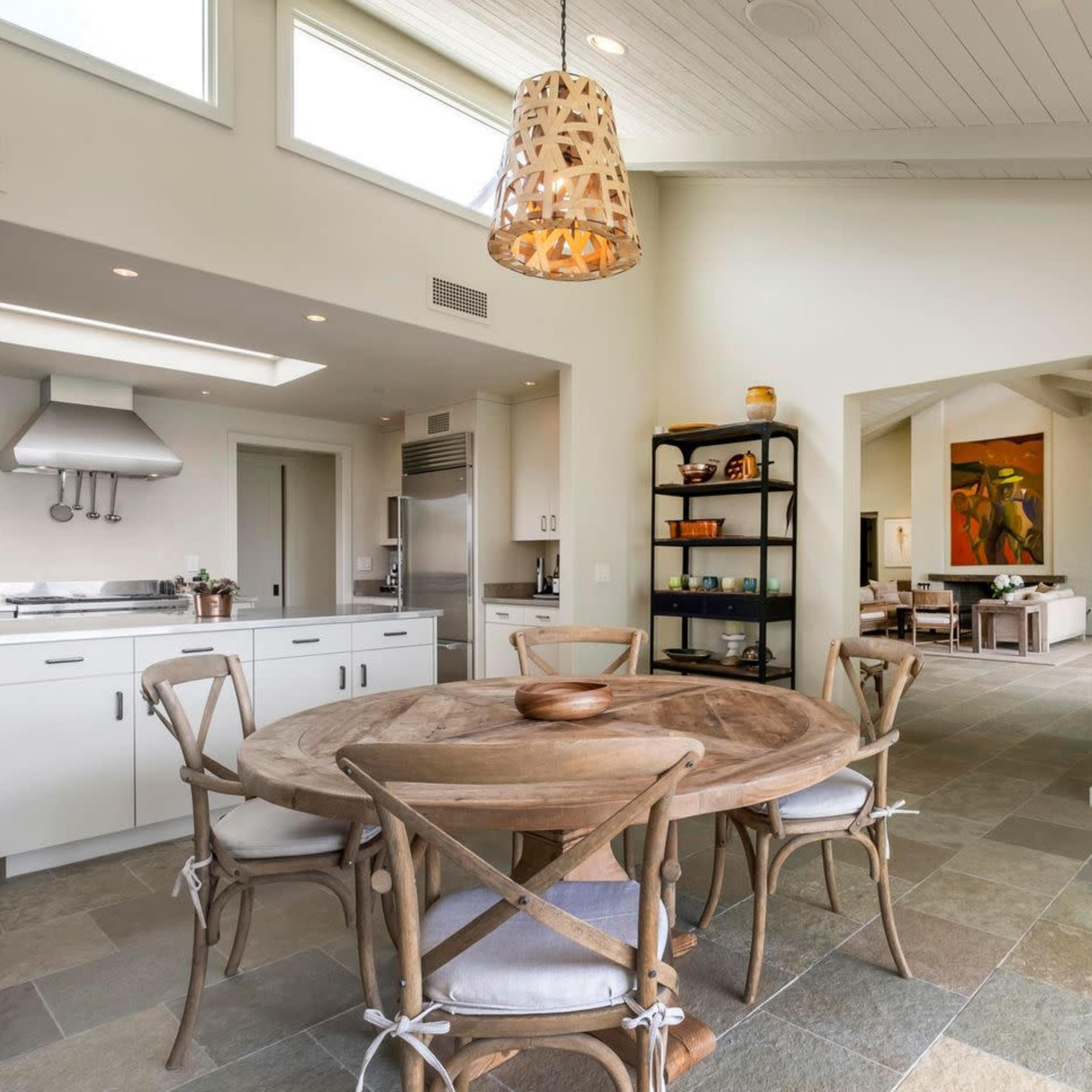 A modern kitchen with a round wooden dining table, surrounded by chairs, and a view of an adjoining living area.