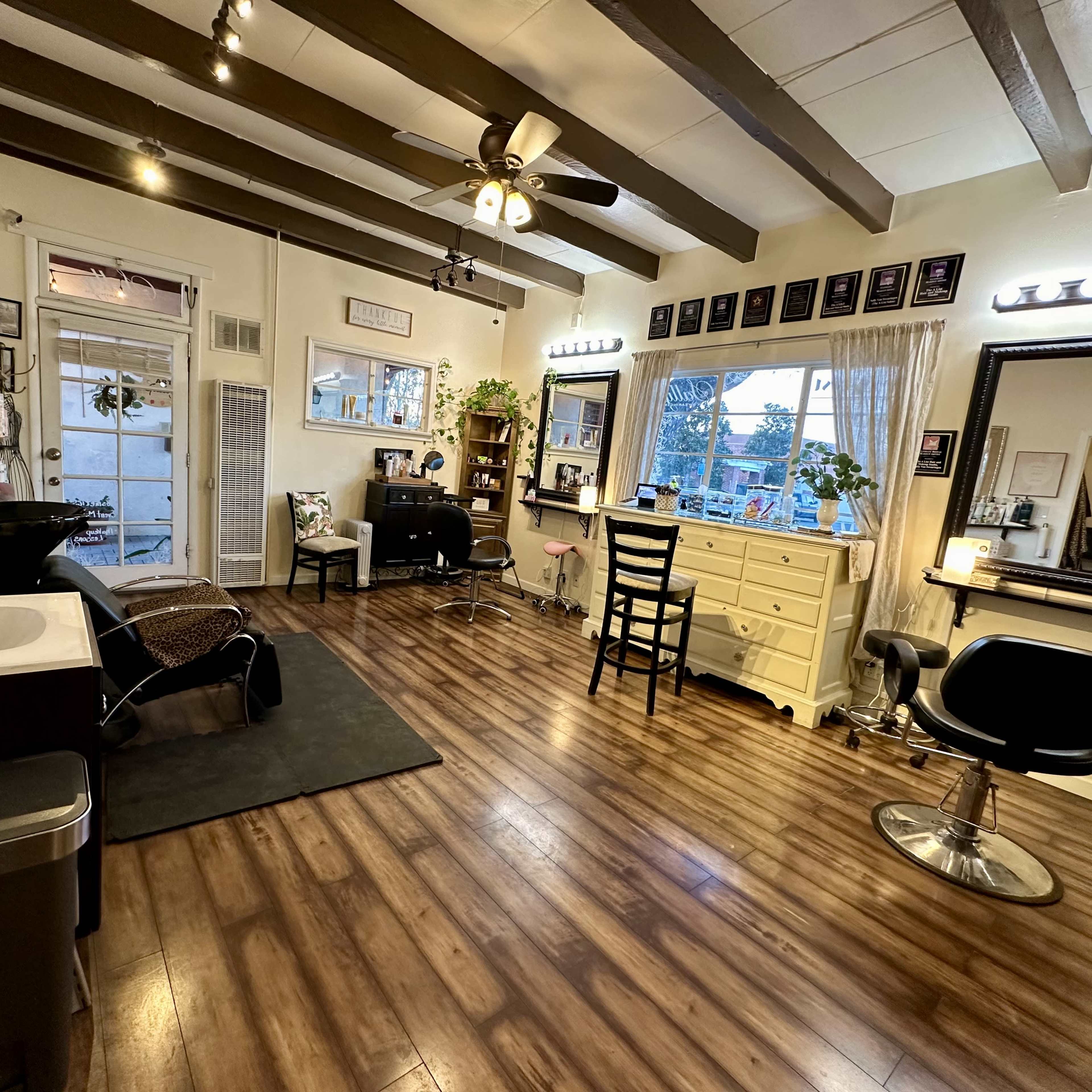 A well-lit hair salon with wooden floors, two styling stations, a sink, and various decor items on the walls.