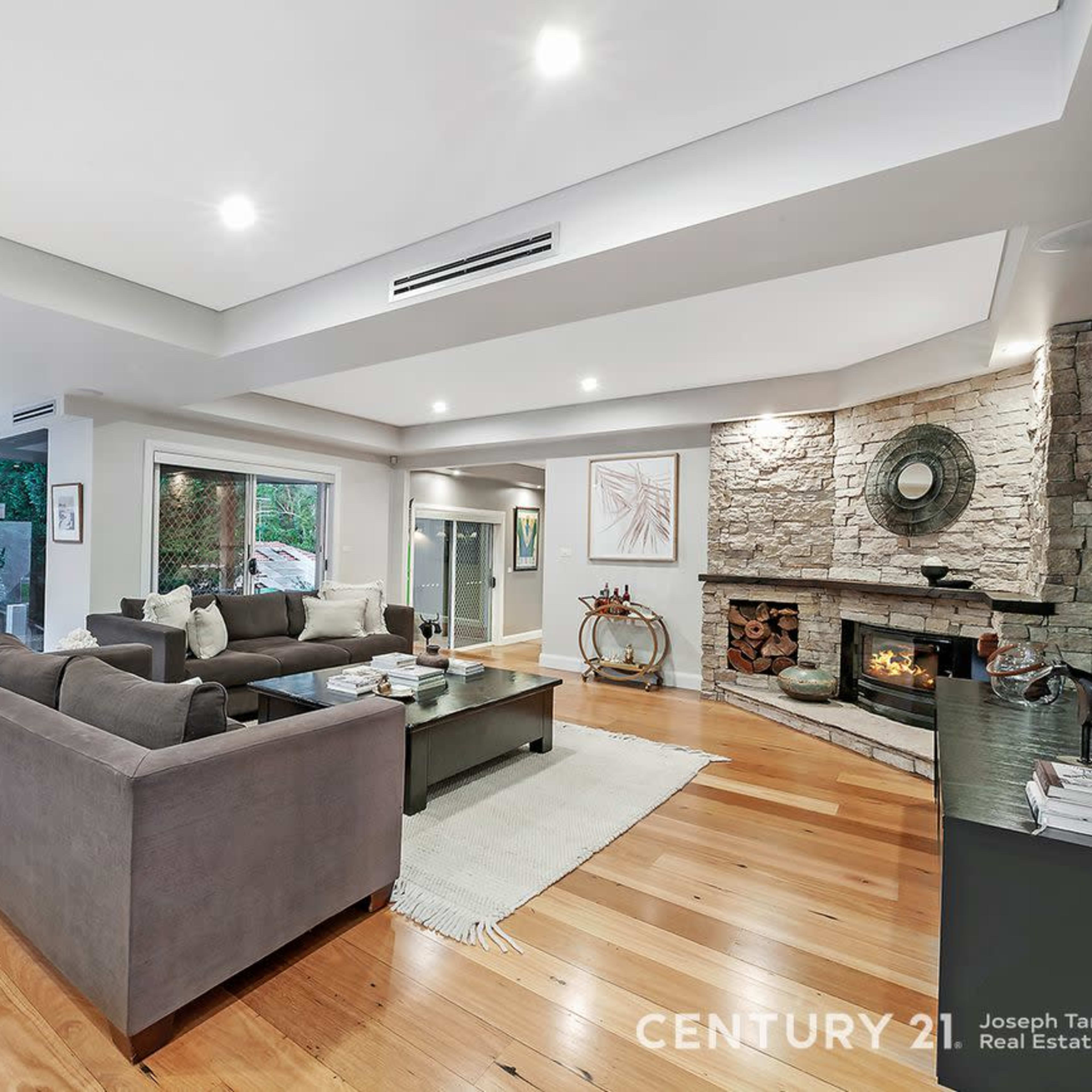 A modern living room and dining area with hardwood floors, large windows, and a stone fireplace.
