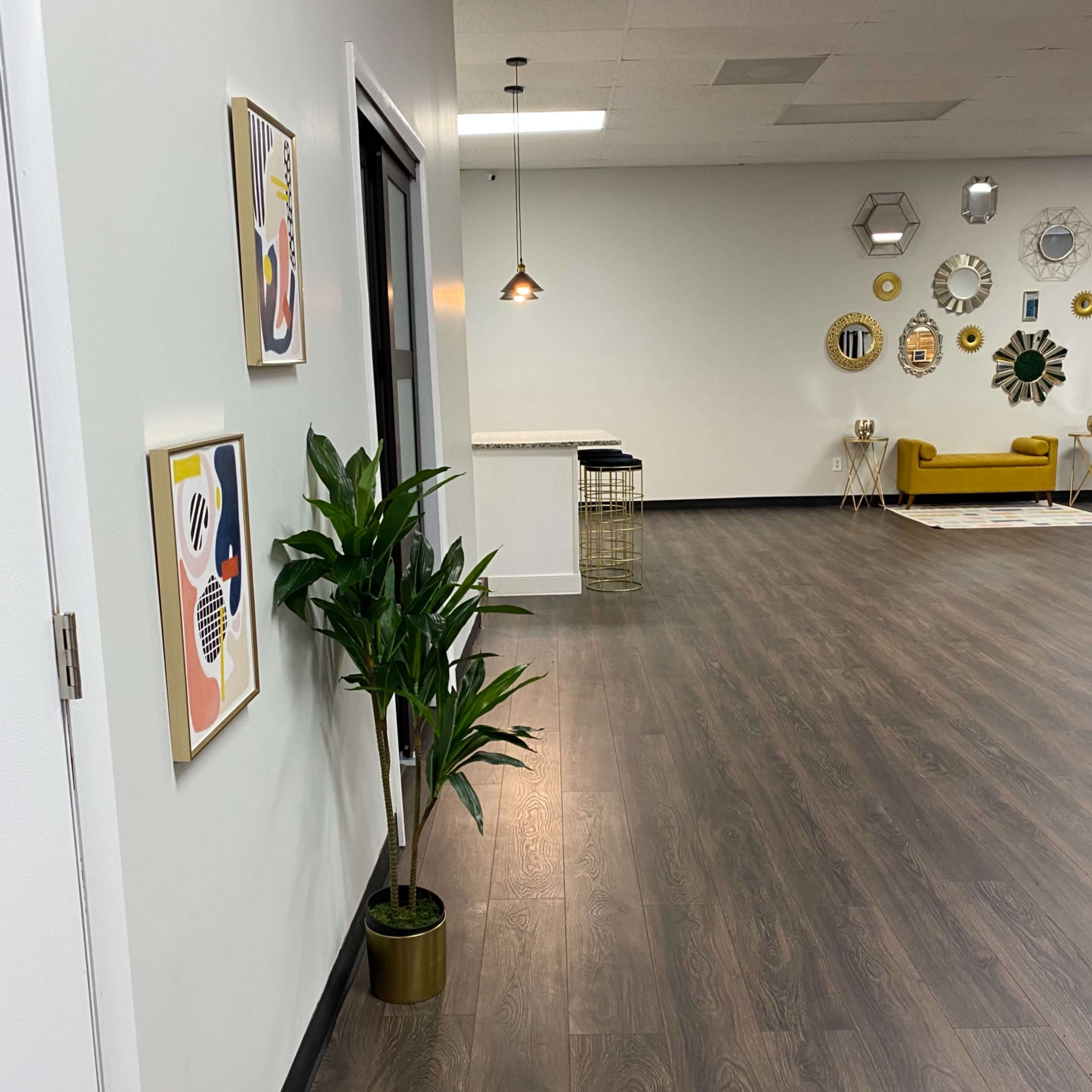 A large, modern interior features a long, open space with wooden flooring, decorative wall art, a potted plant, and a seating area against a wall with circular decorations.