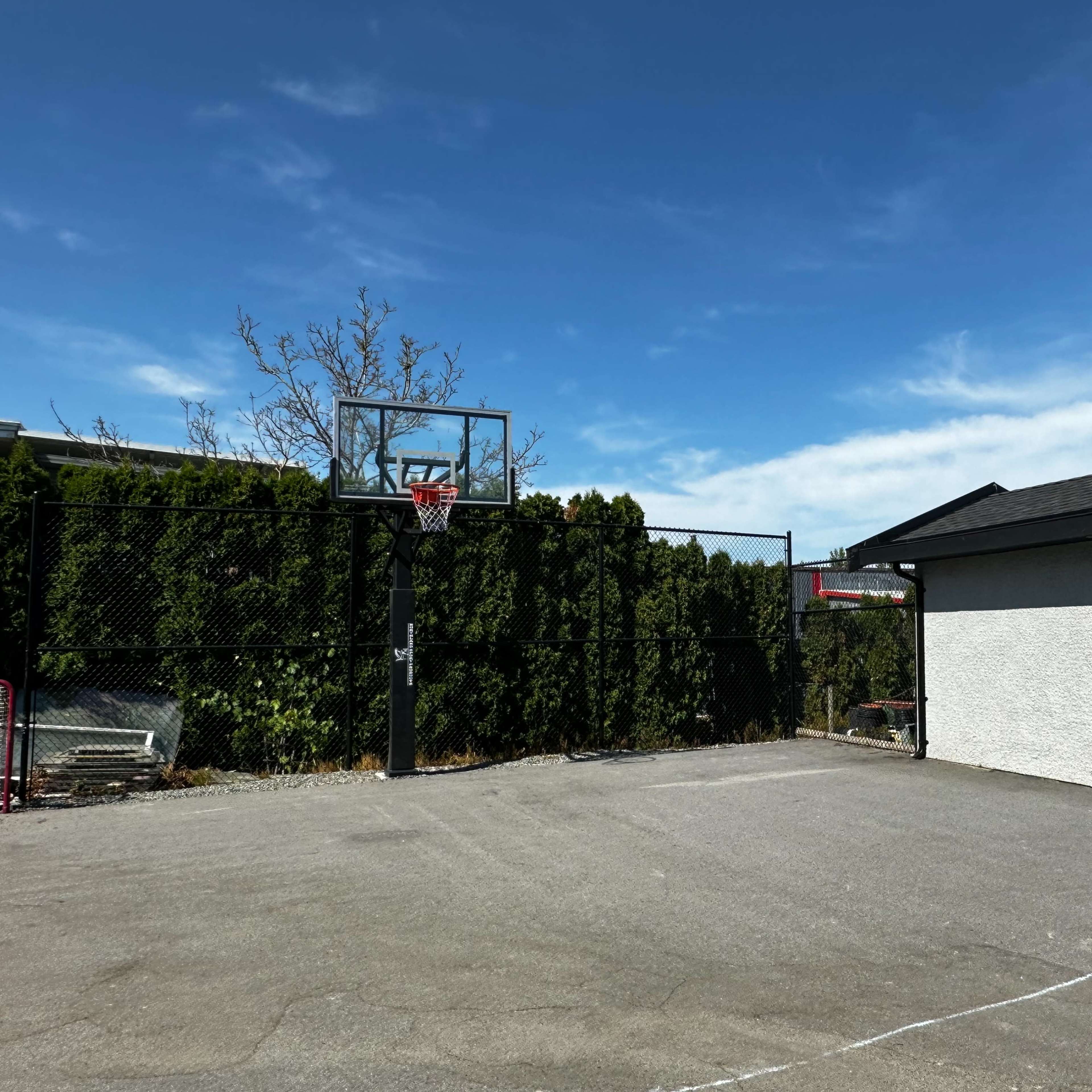 A fenced outdoor basketball court with a hoop and a small building nearby.