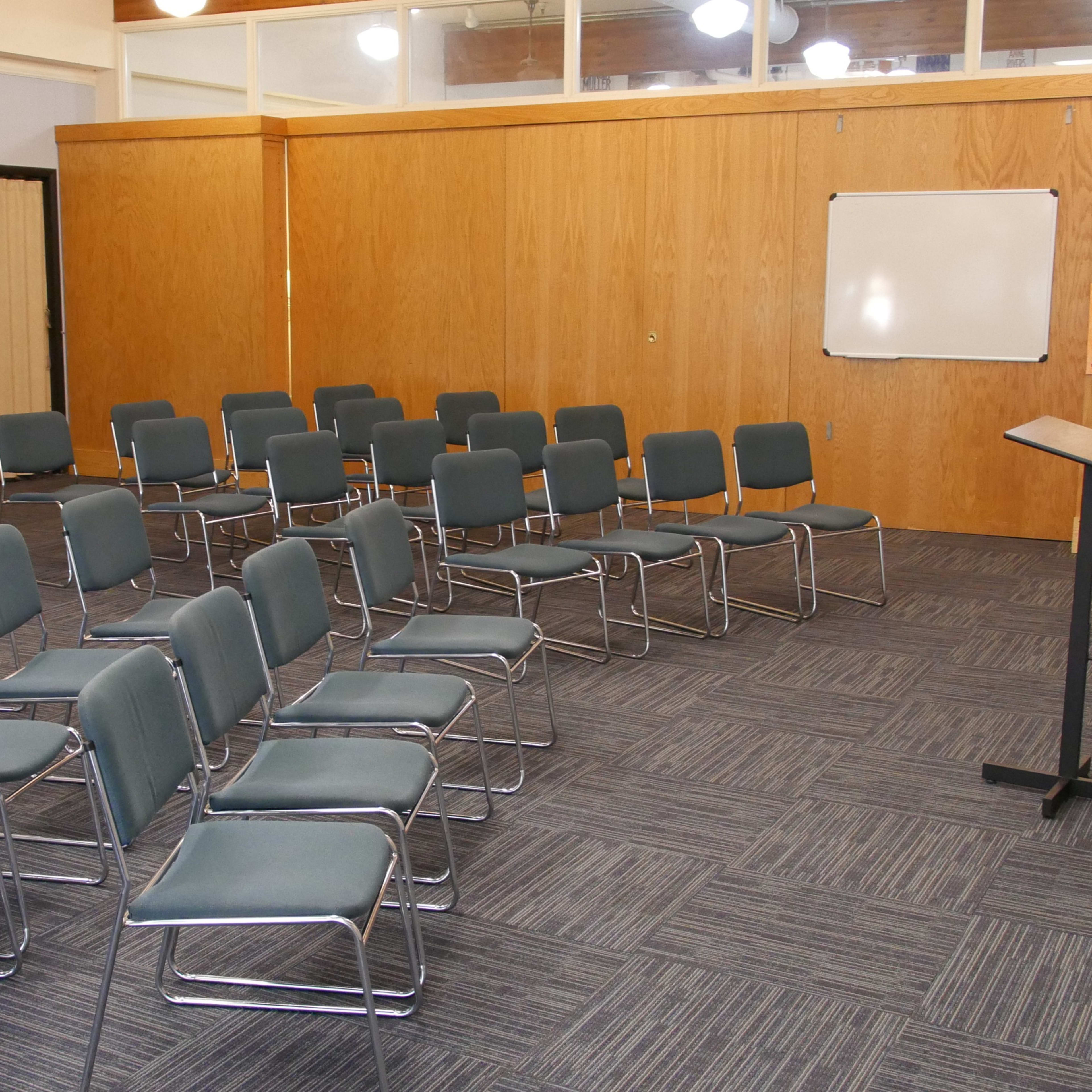 A room with neatly arranged gray chairs facing a podium, accompanied by colorful artwork on the walls.