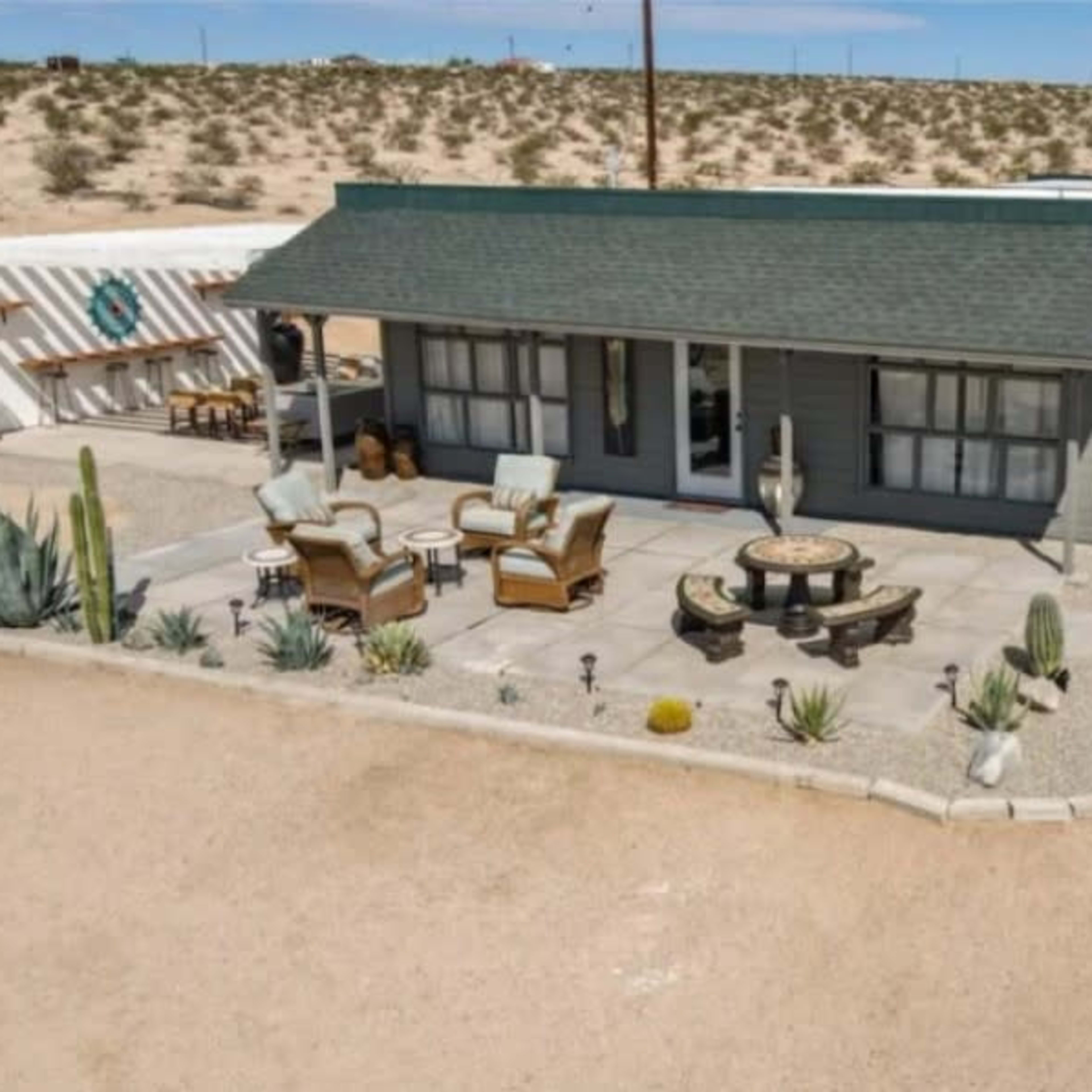 A desert property featuring a single-story house with a porch, surrounded by landscaped gravel and desert plants.