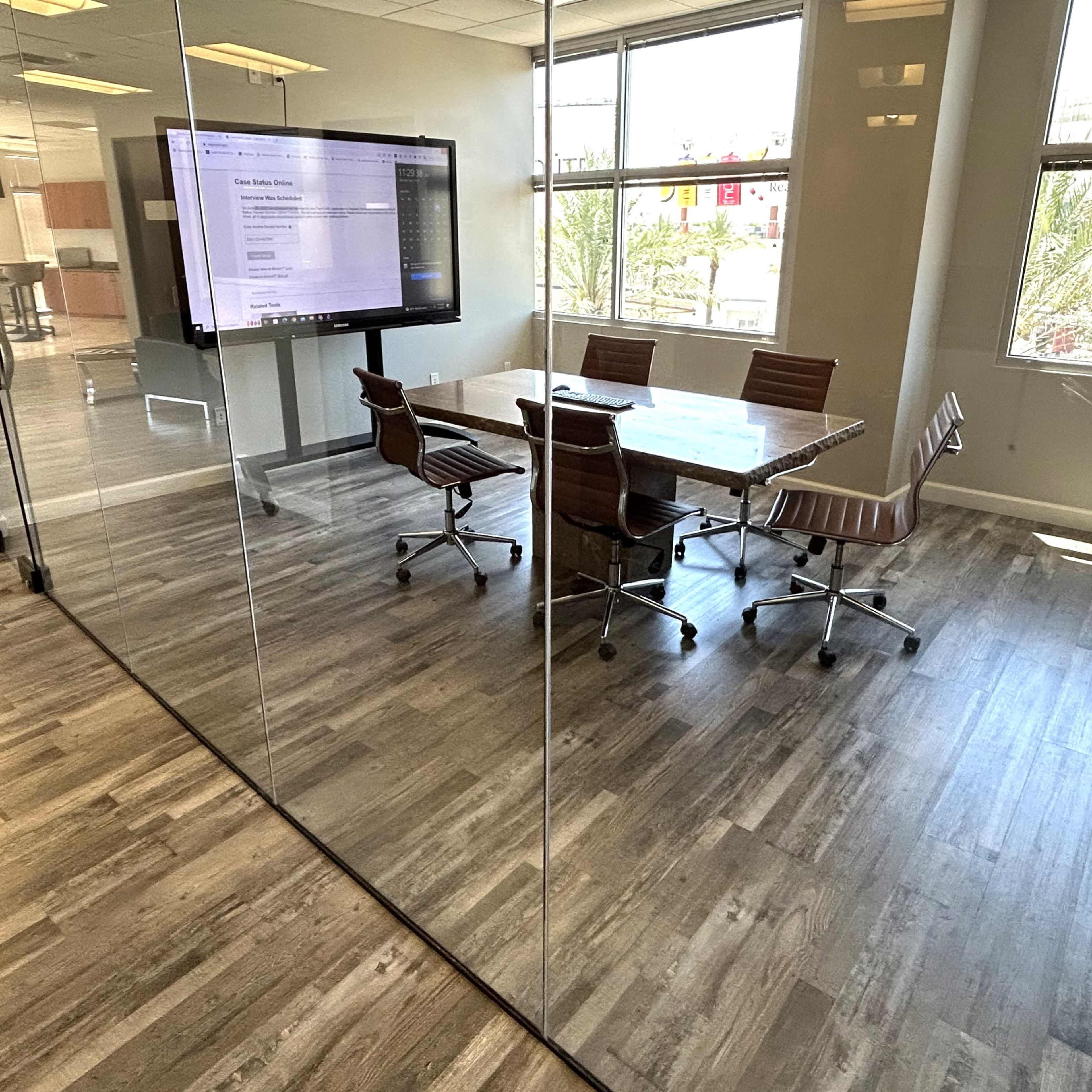 A modern conference room with a glass wall, a wooden table, and four brown office chairs.