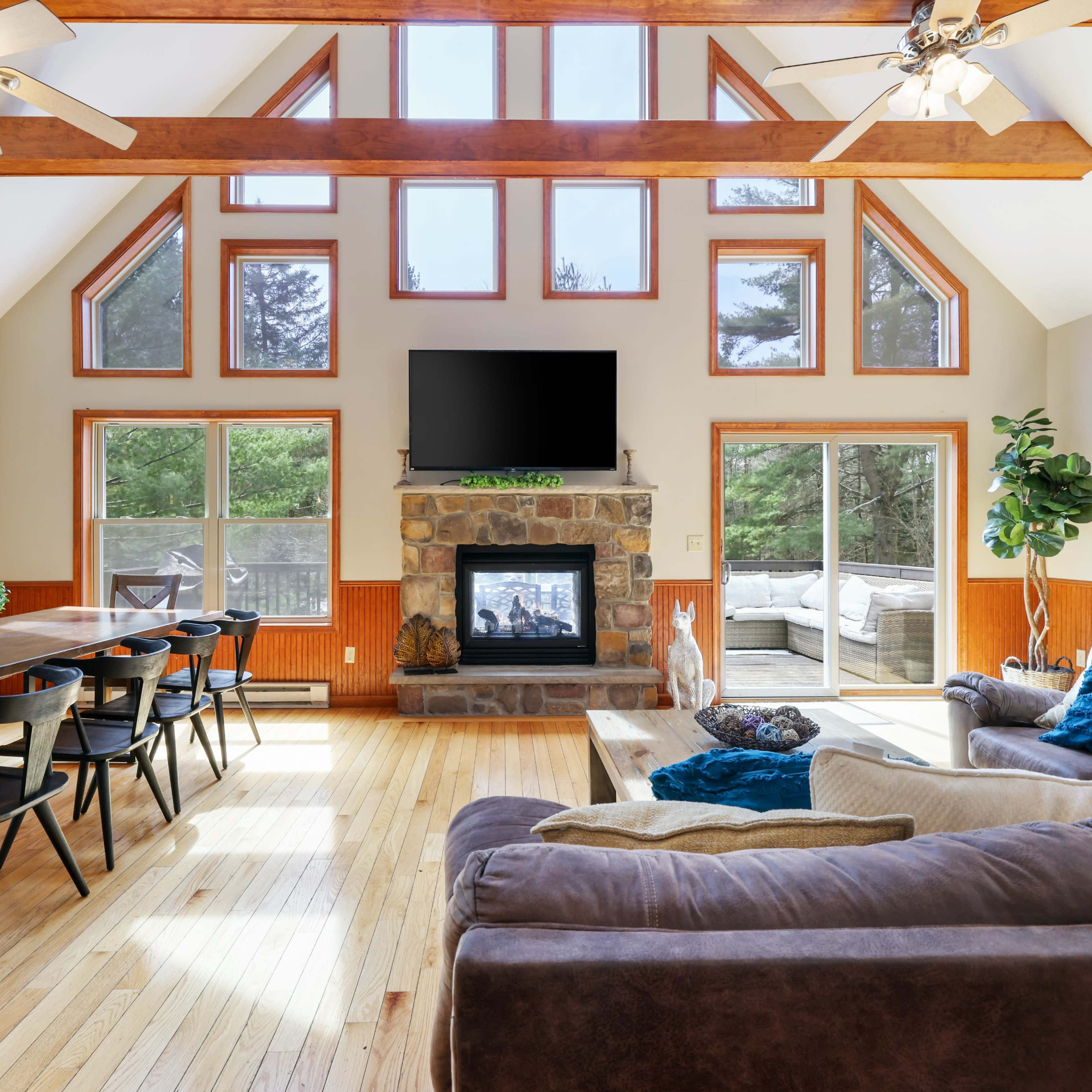 A spacious living room features large windows, a stone fireplace, and a dining area with a long table.