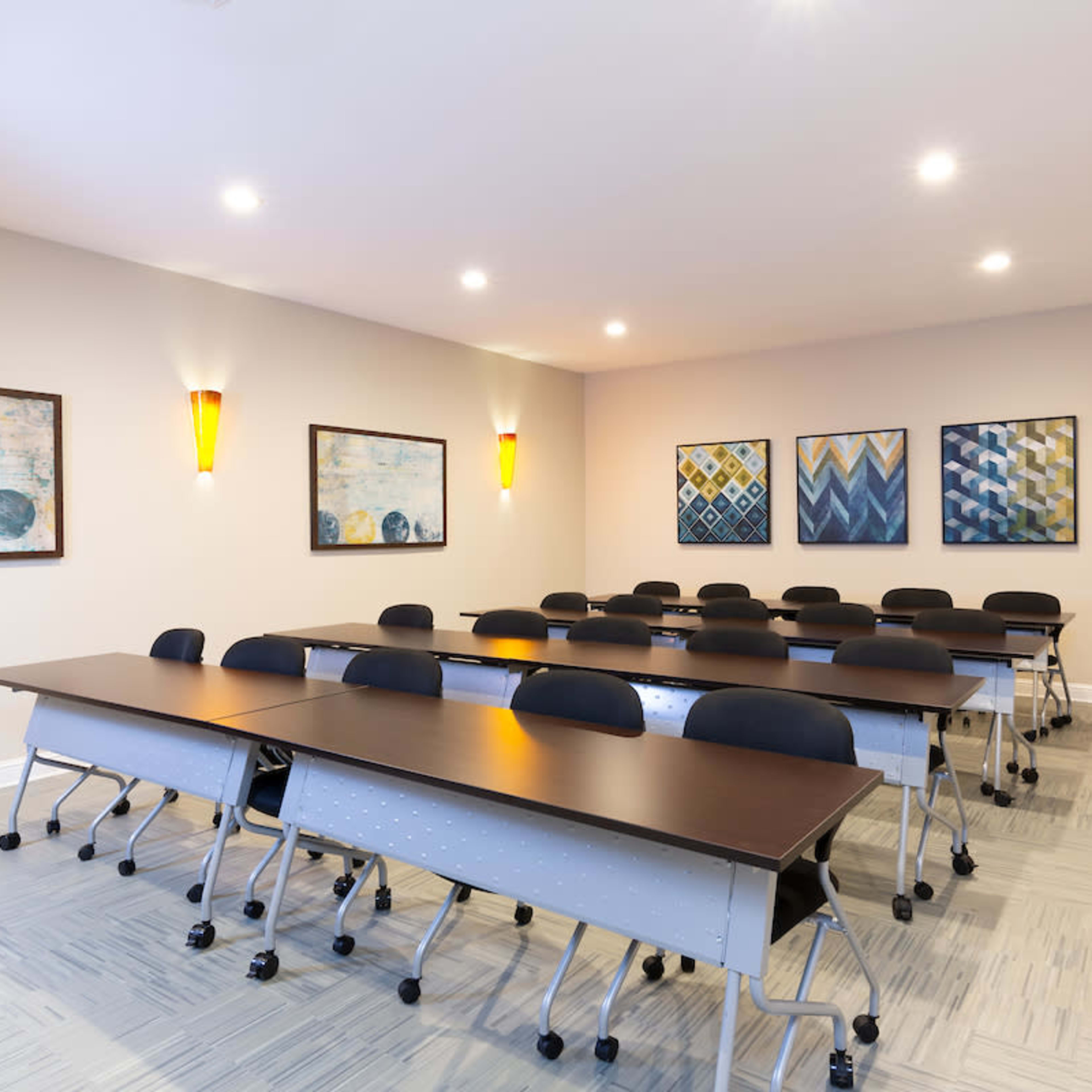 A spacious conference room arranged with multiple rows of black chairs and long tables, featuring decorative art on the walls.