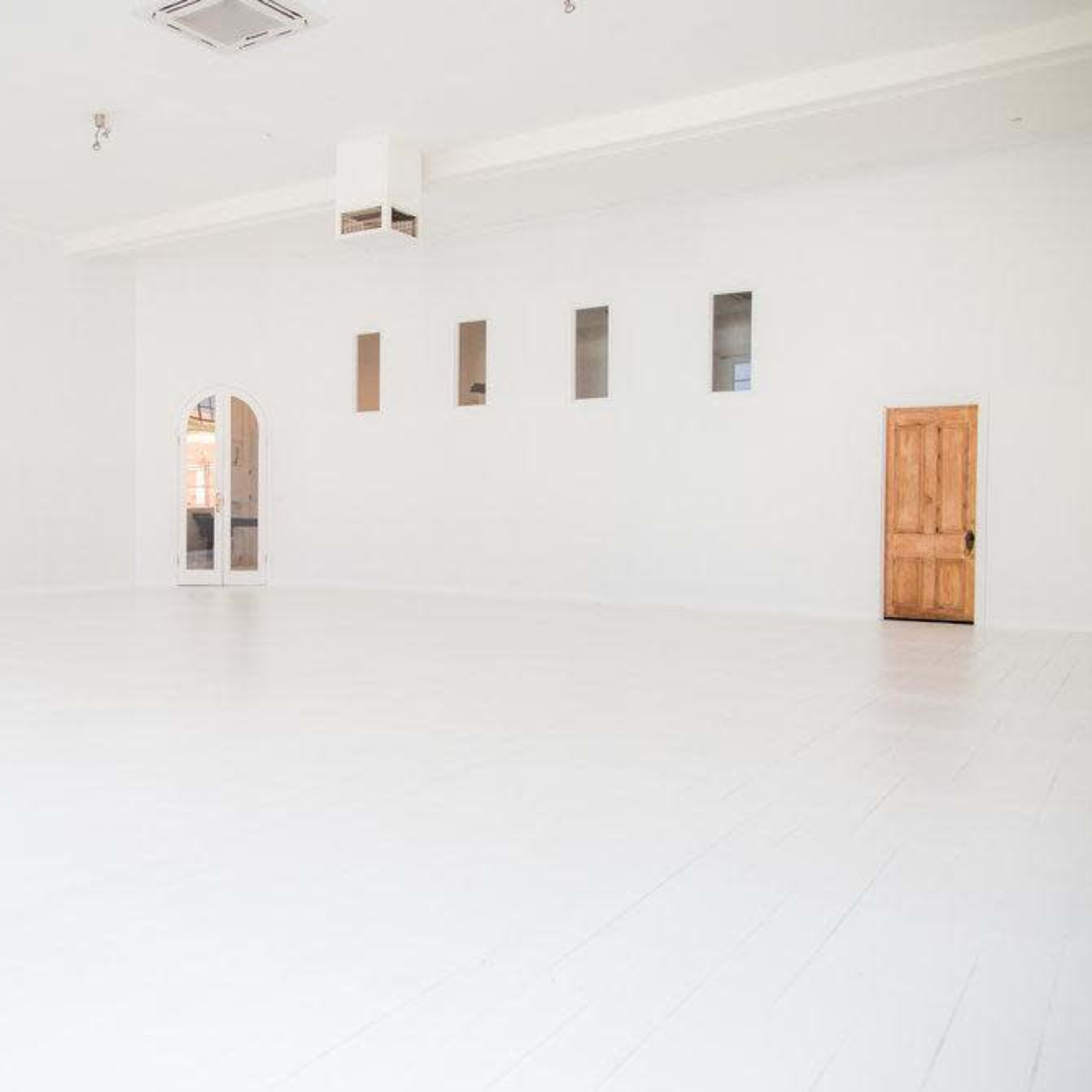 A spacious, empty room with white walls, a wooden door, and several small windows.