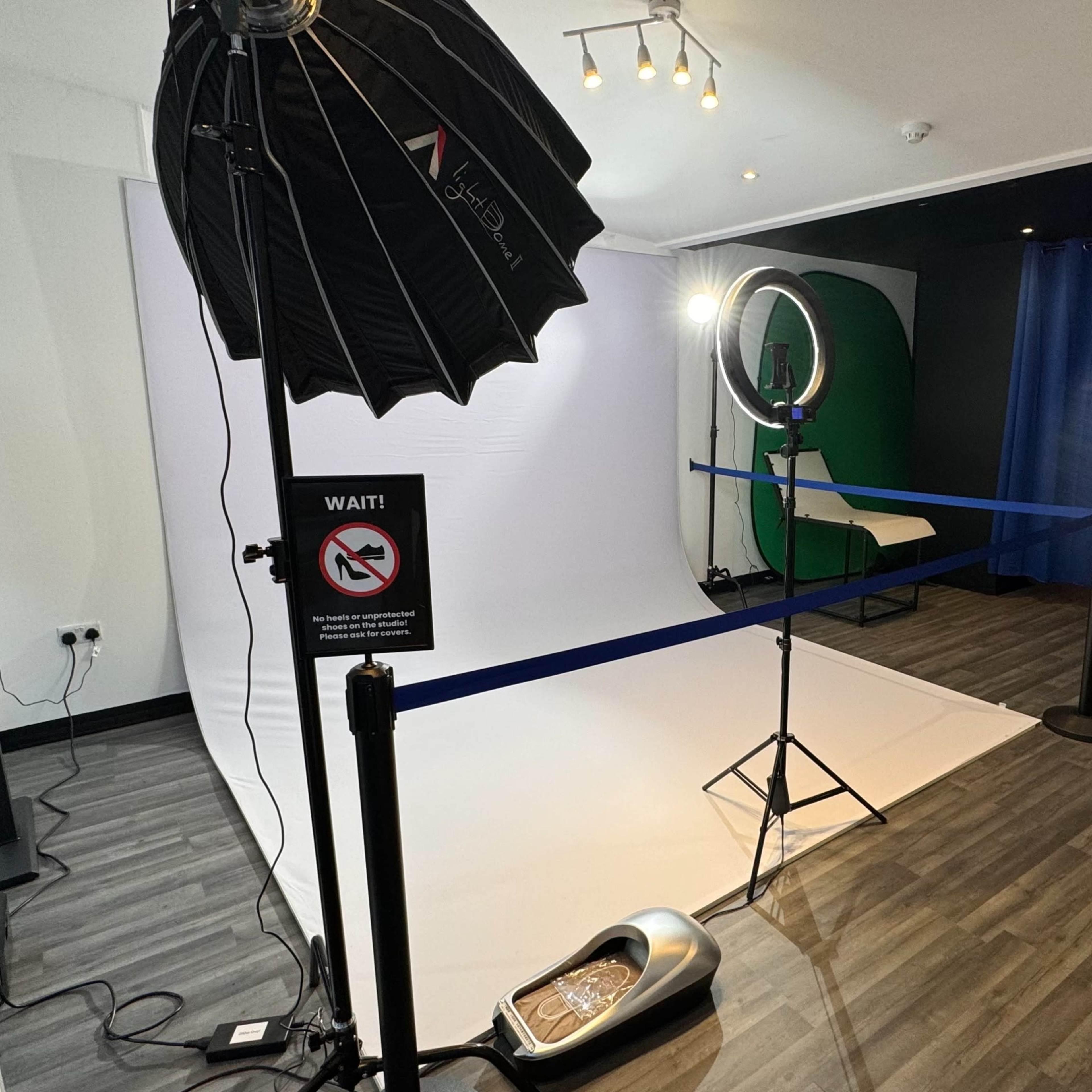 A photo studio setup with a white backdrop, ring light, softbox, and a blue curtain in the background.
