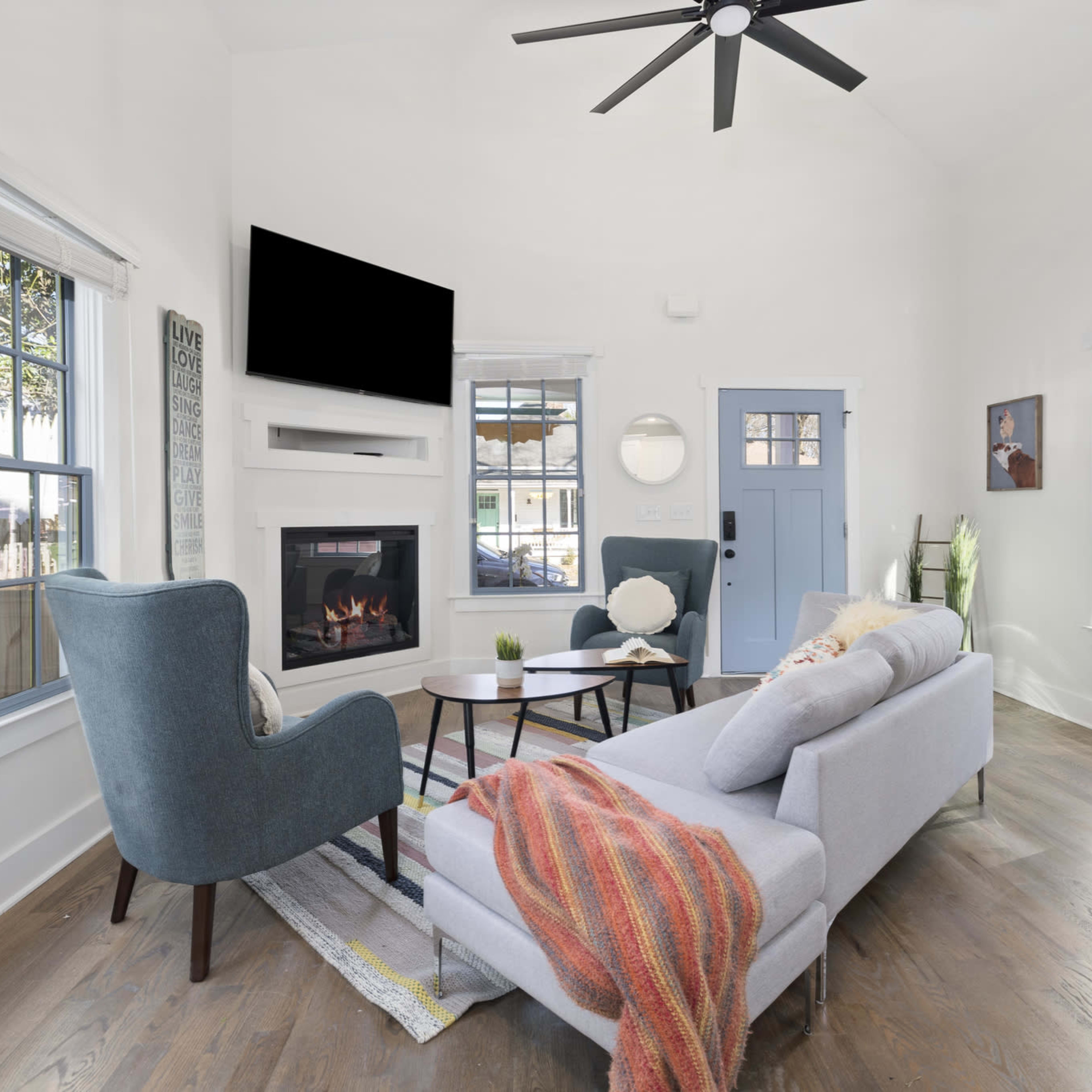 A modern living room with a sectional sofa, a coffee table, and a blue front door, featuring a fireplace and large windows.