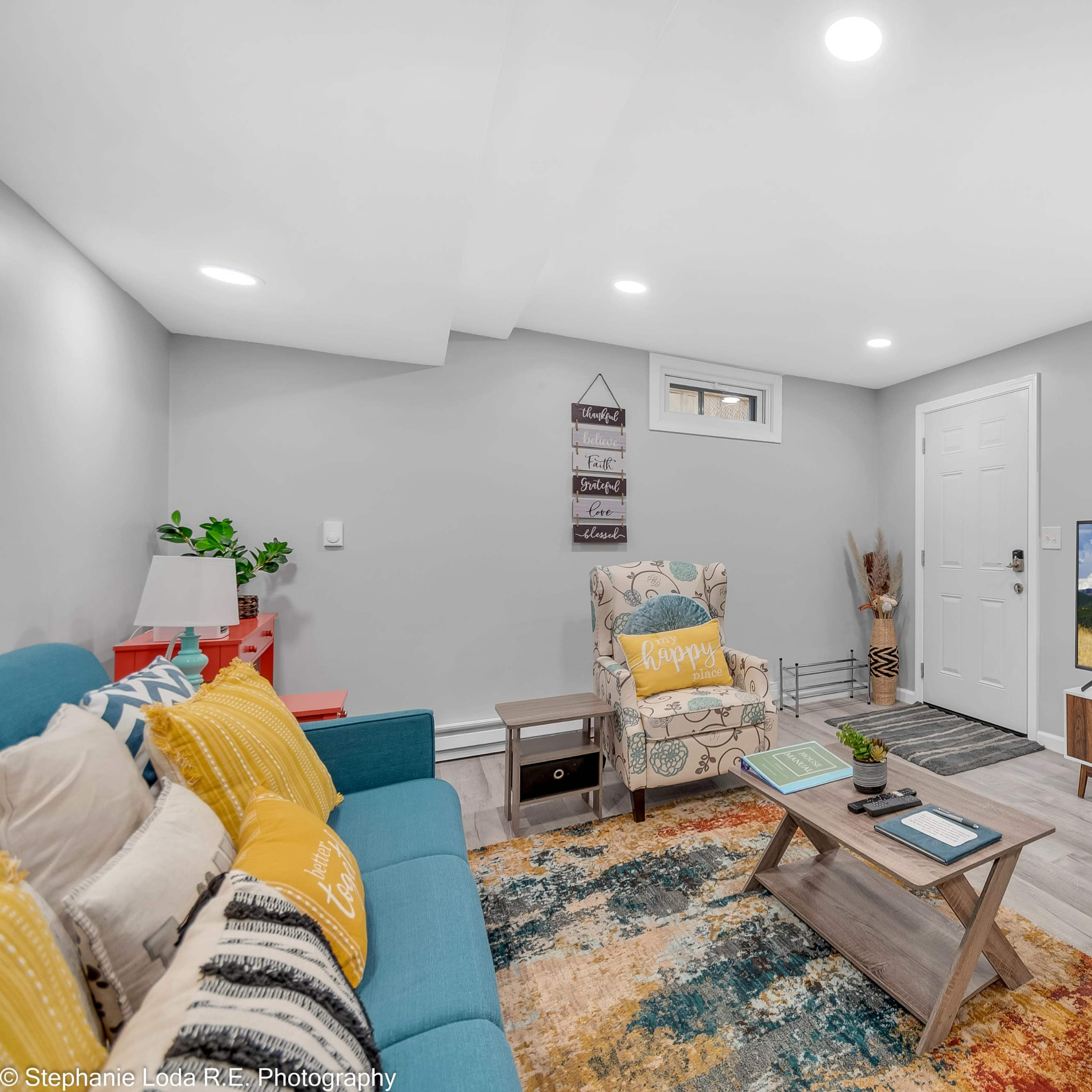 The room features a cozy seating area with colorful chairs, a coffee table, and a television against a light gray wall.